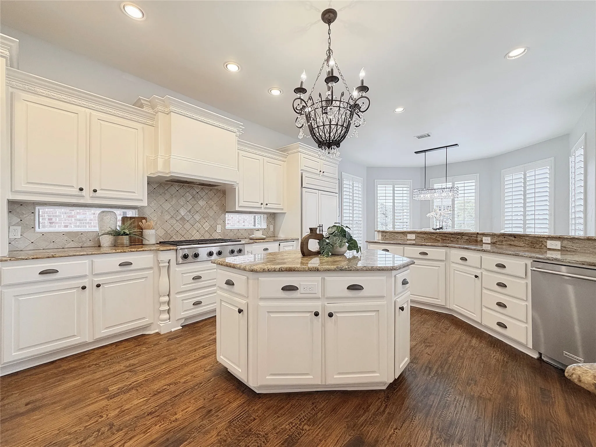 Kitchen with light stone counters, hanging light fixtures, appliances with stainless steel finishes, a kitchen island, and dark wood-style floors
