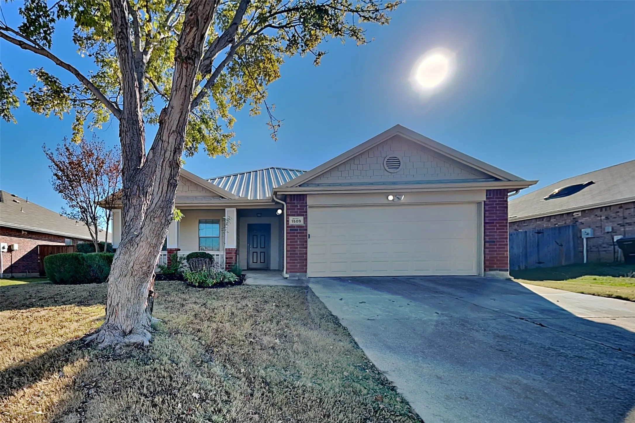 Ranch-style home featuring driveway, brick siding, a metal roof, and a garage