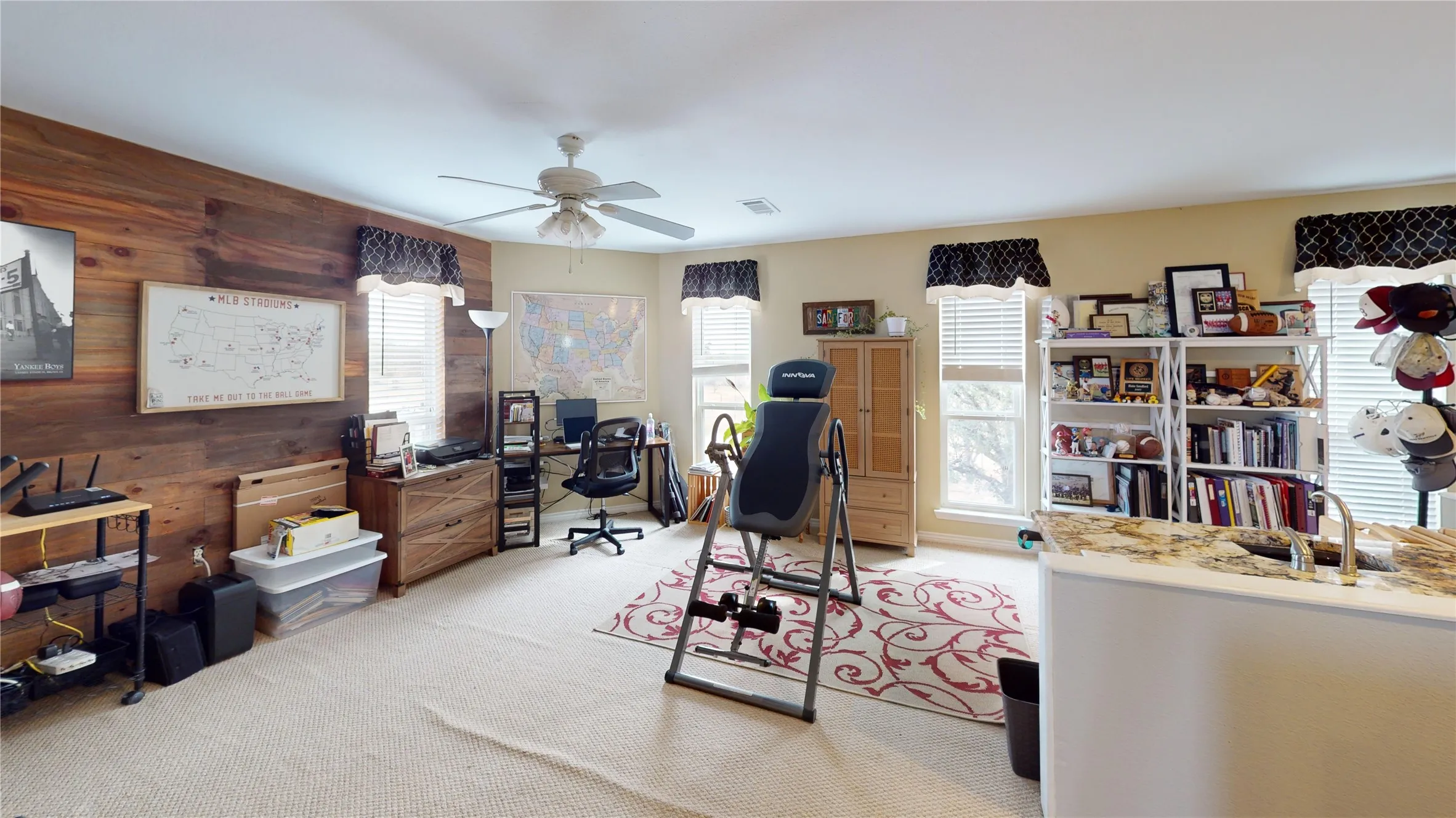 Office area featuring wooden walls, light colored carpet, and ceiling fan
