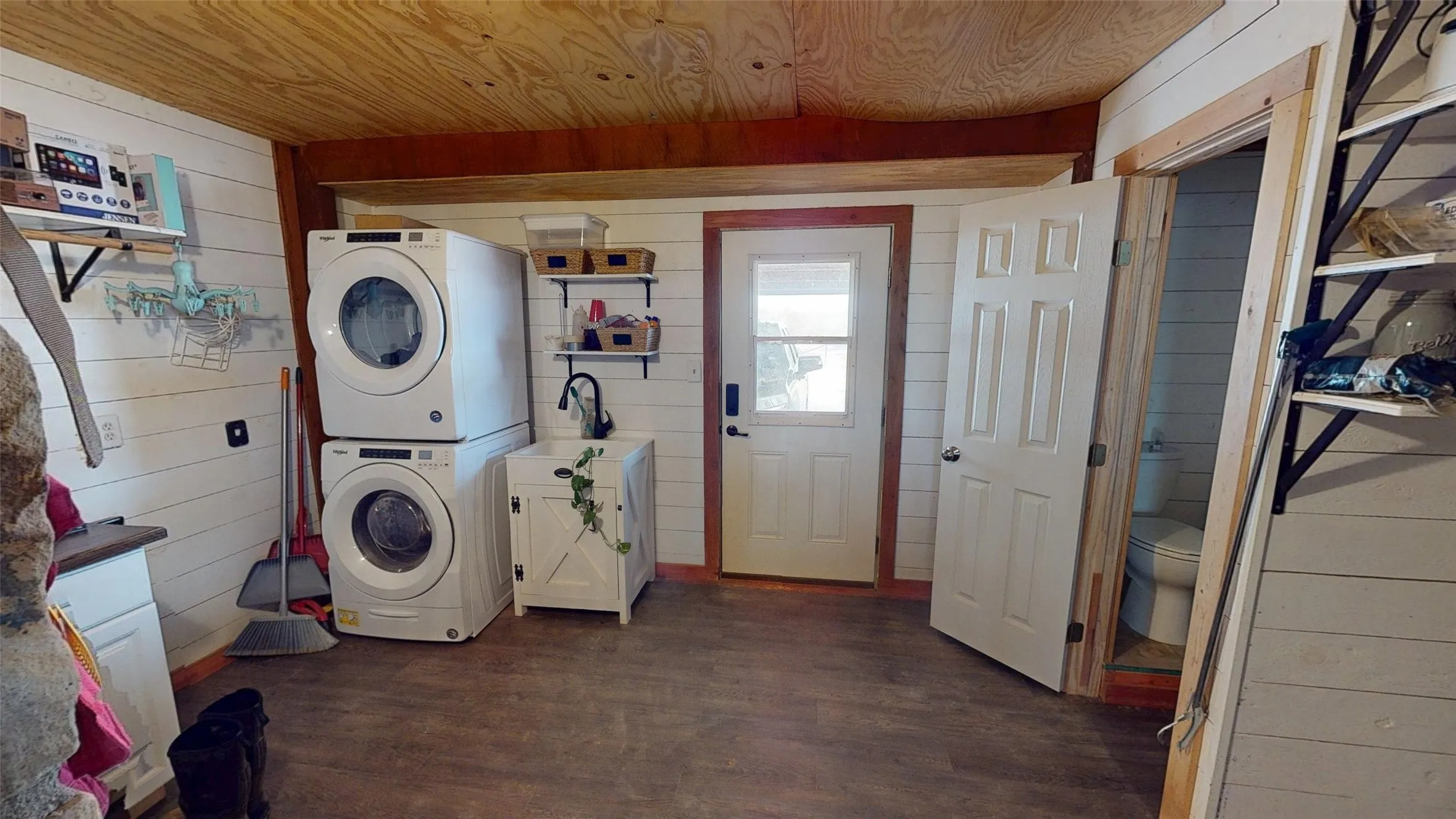 Washroom with wood walls, wood ceiling, dark wood-style flooring, and stacked washer / drying machine