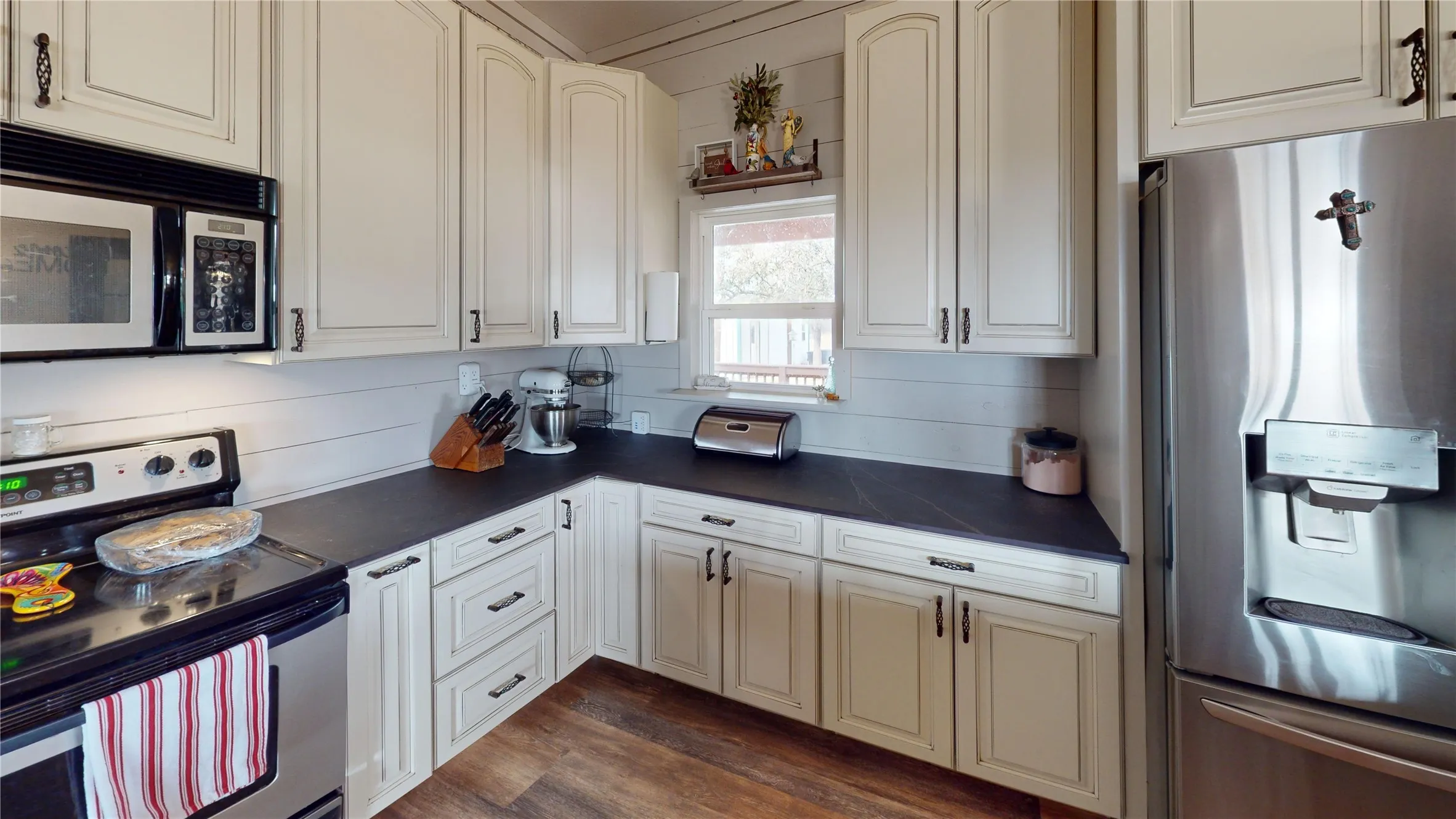 Kitchen with appliances with stainless steel finishes, dark countertops, dark wood-style floors, and cream cabinetry