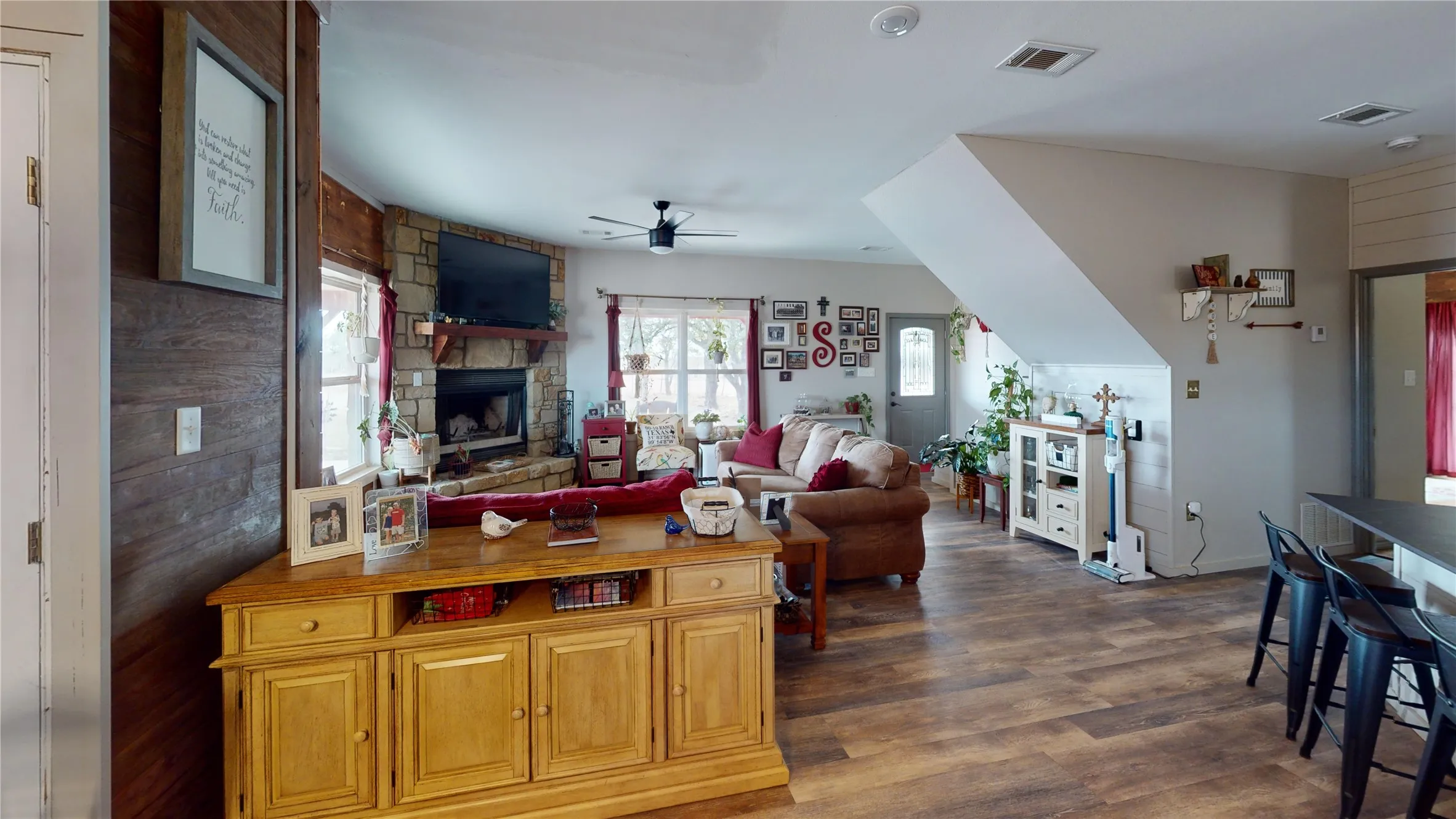 Living area featuring dark wood-style floors, a ceiling fan, a stone fireplace, and wooden walls