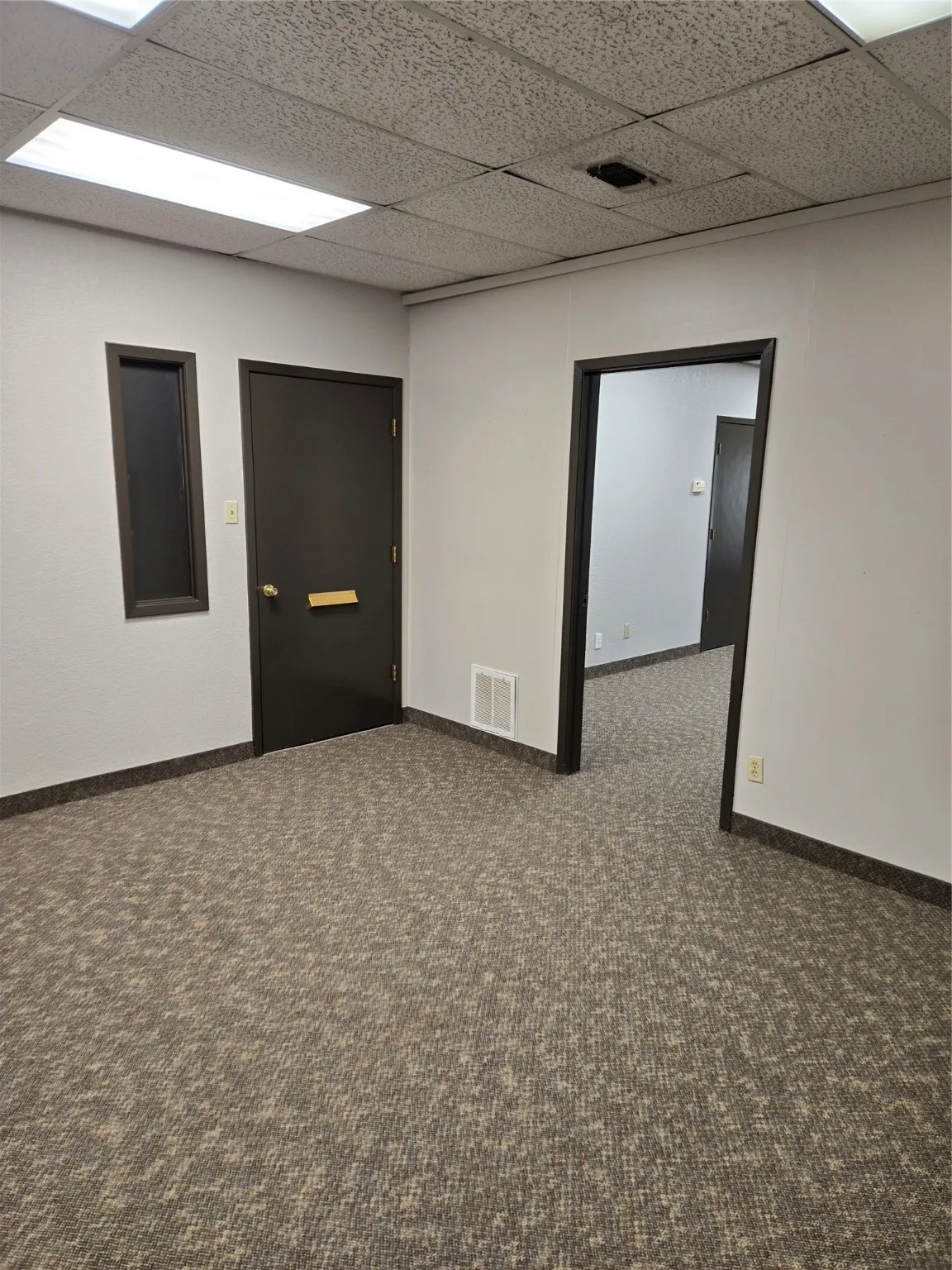 Unfurnished room with a drop ceiling and dark colored carpet