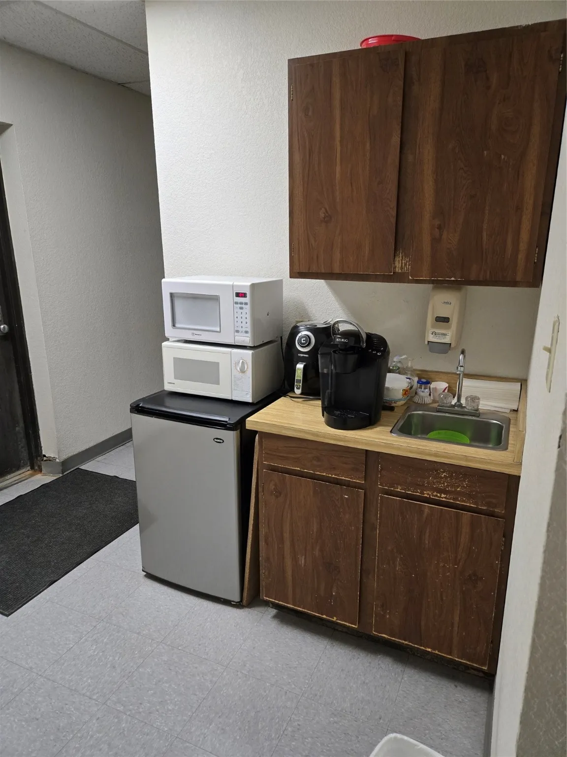 Kitchen with dark brown cabinets, a textured wall, light countertops, white refrigerator, and a paneled ceiling