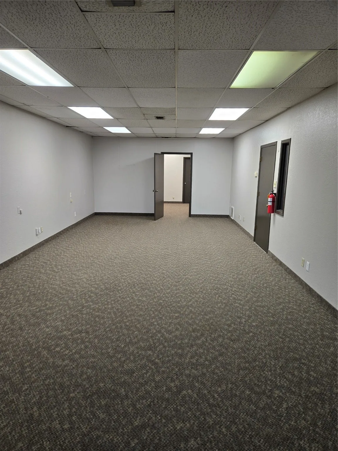 Carpeted spare room featuring baseboards and a drop ceiling
