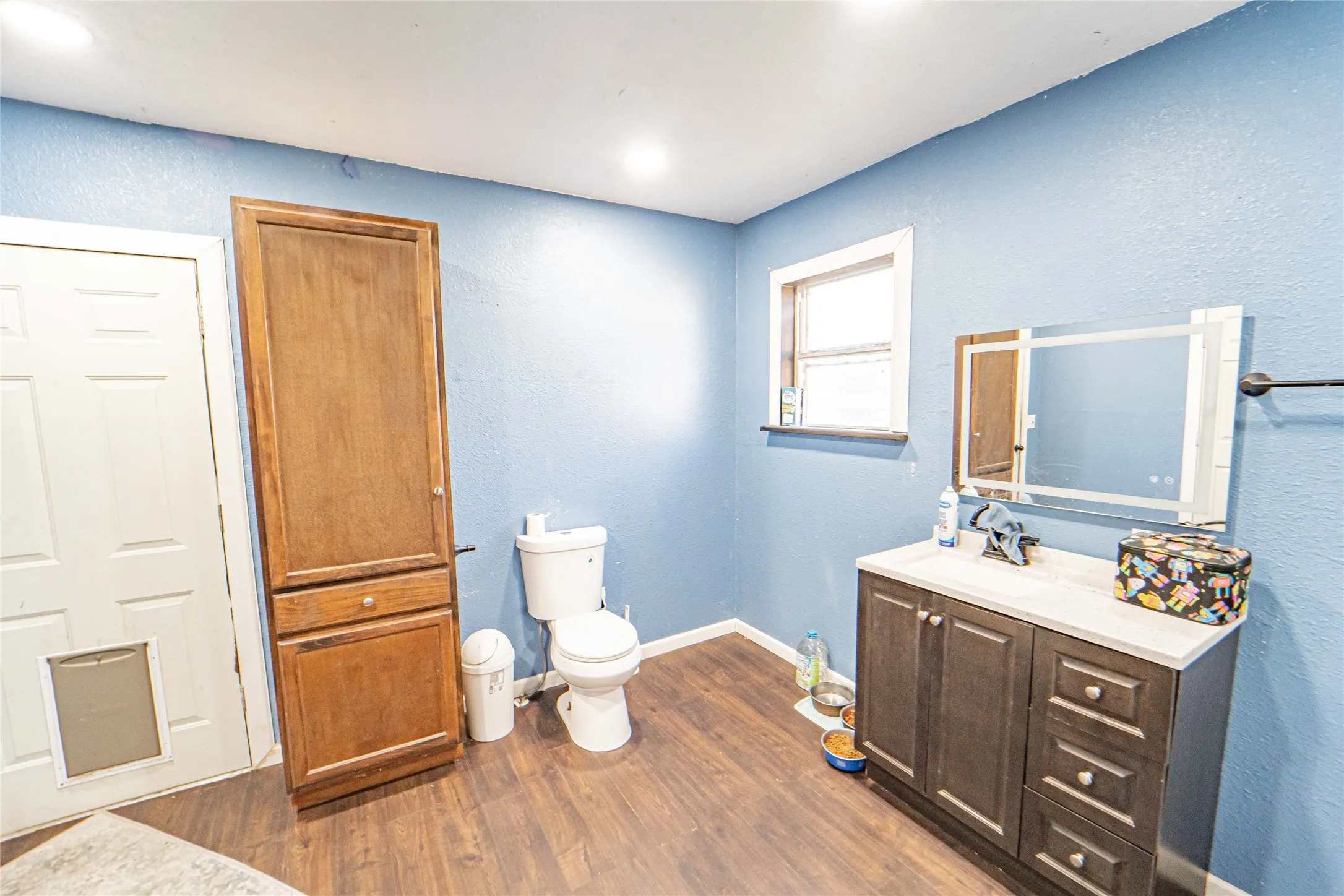 Full bathroom with a textured wall, dark wood-style floors, and vanity