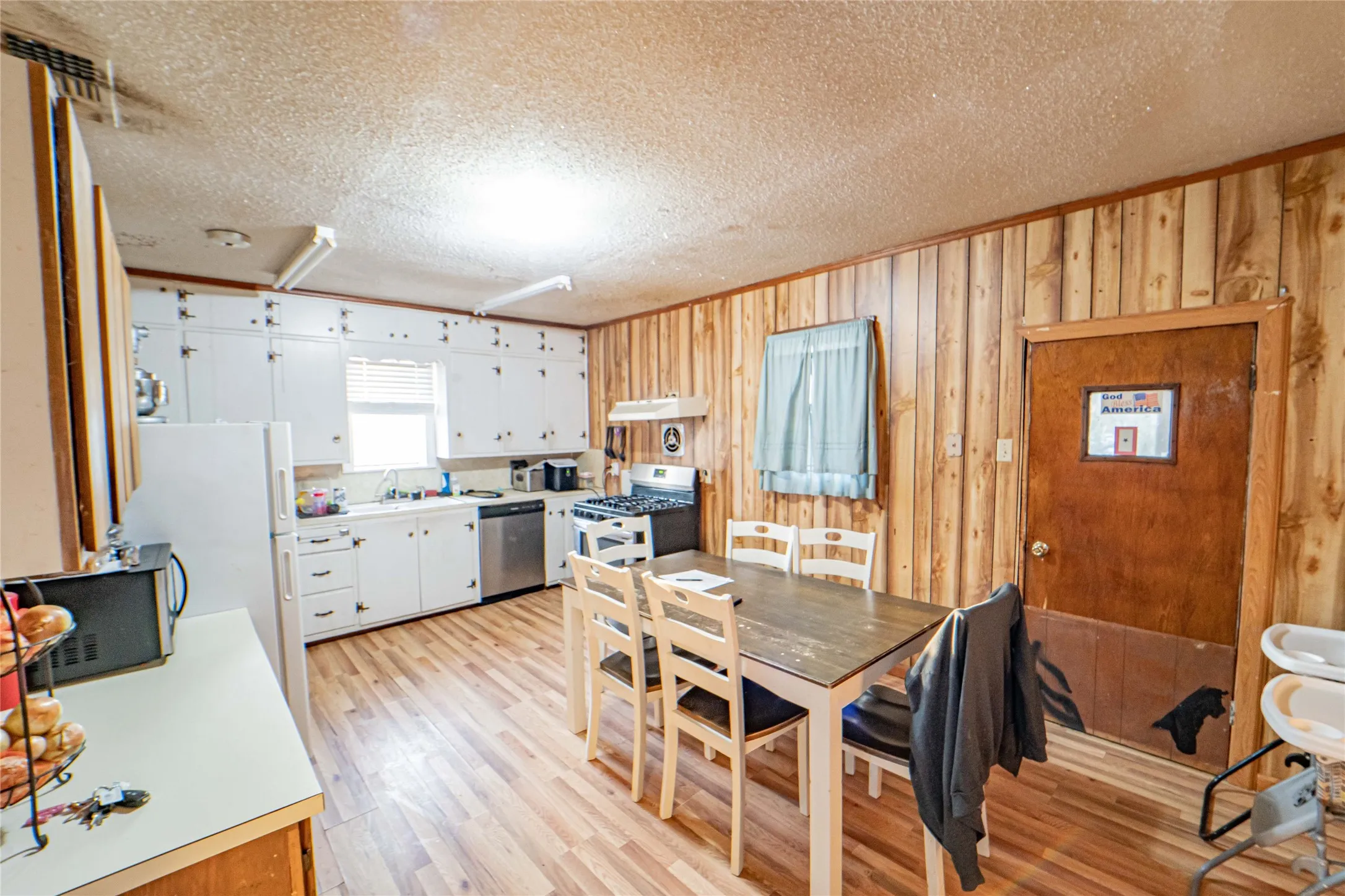 Dining area featuring a textured ceiling, wooden walls, light wood-style flooring, and ornamental molding