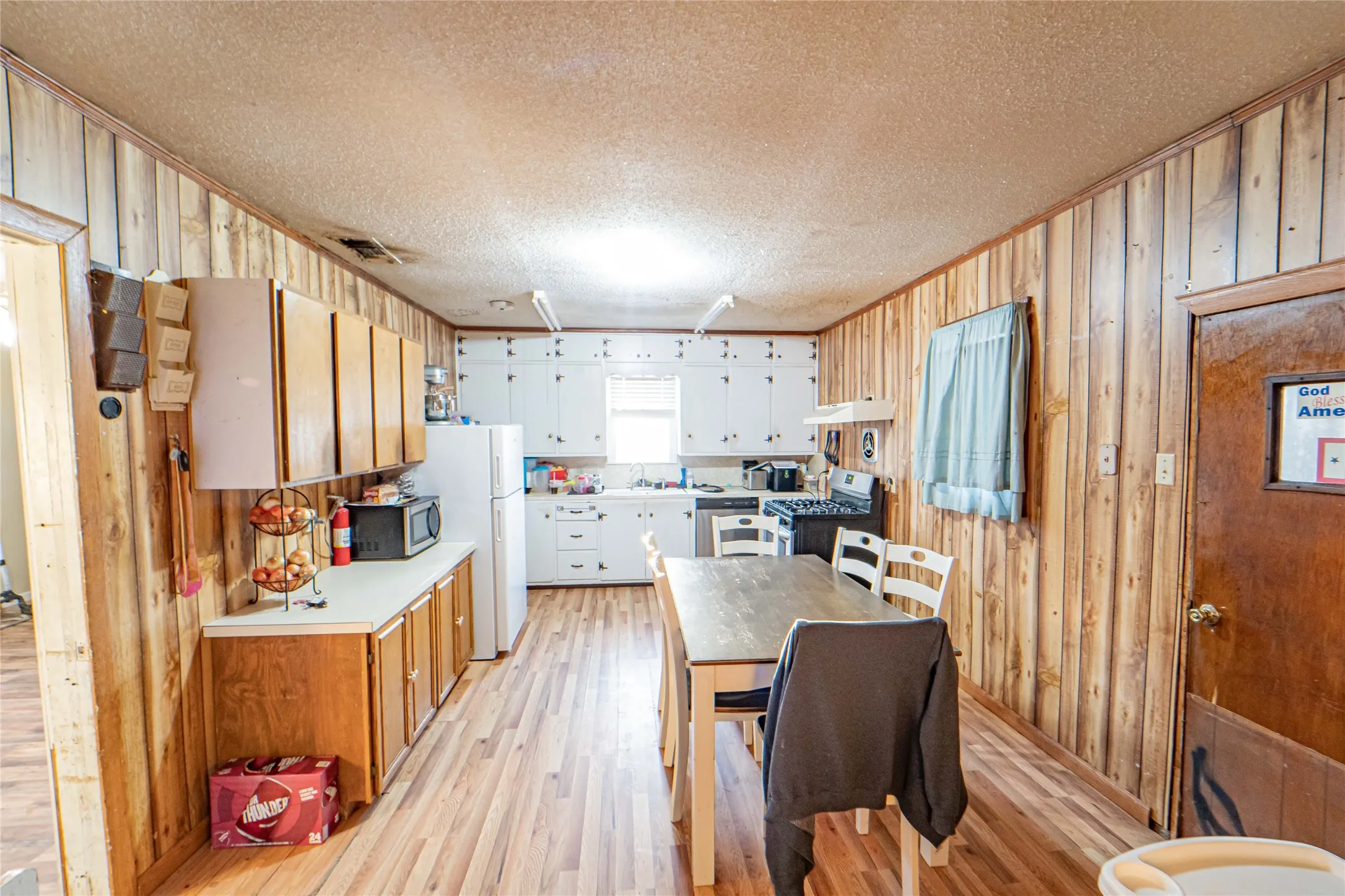 Kitchen featuring light countertops, wooden walls, light wood-type flooring, white cabinetry, and a textured ceiling
