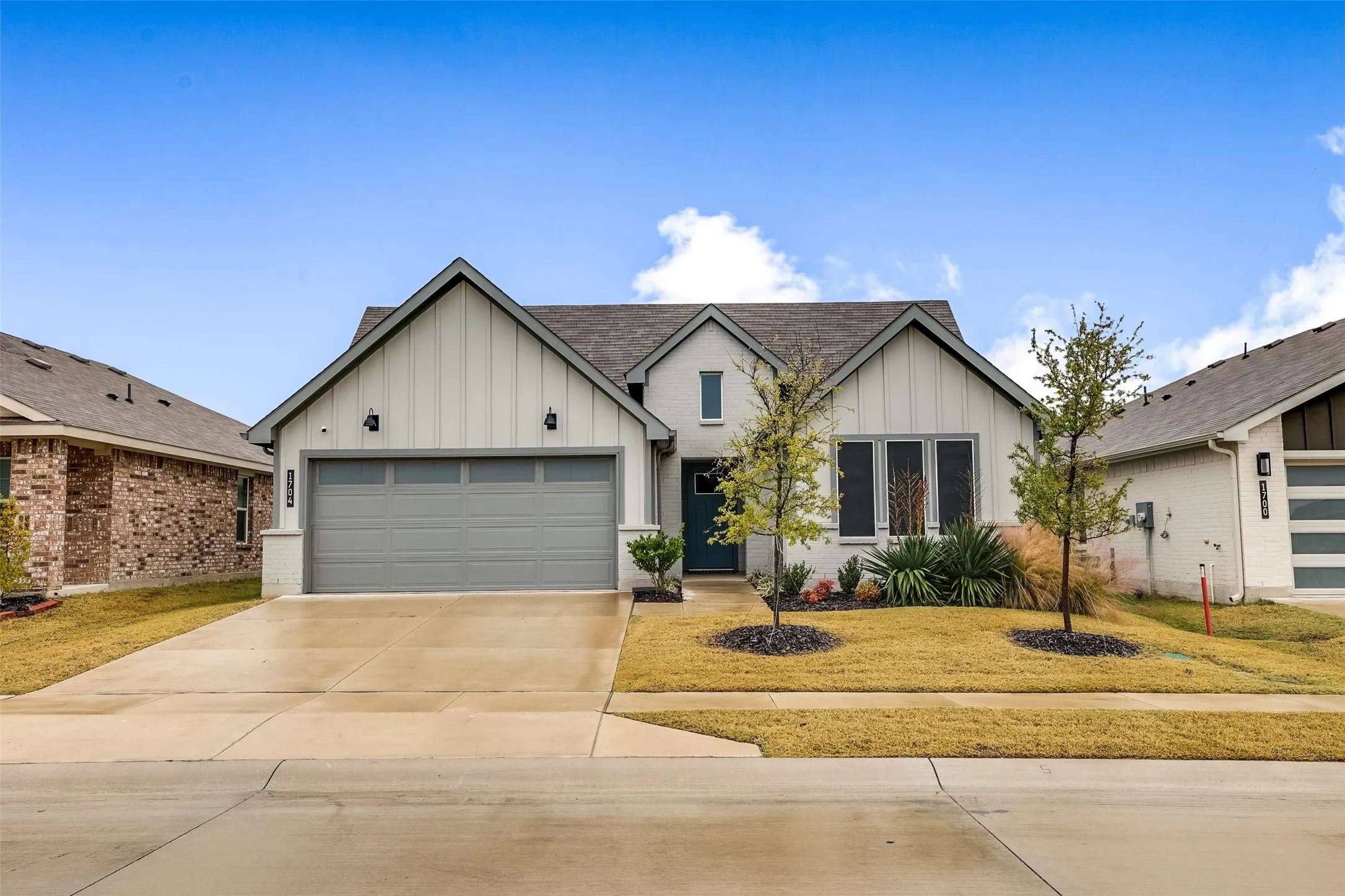 View of front facade with board and batten siding, driveway, an attached garage, roof with shingles, and a front yard