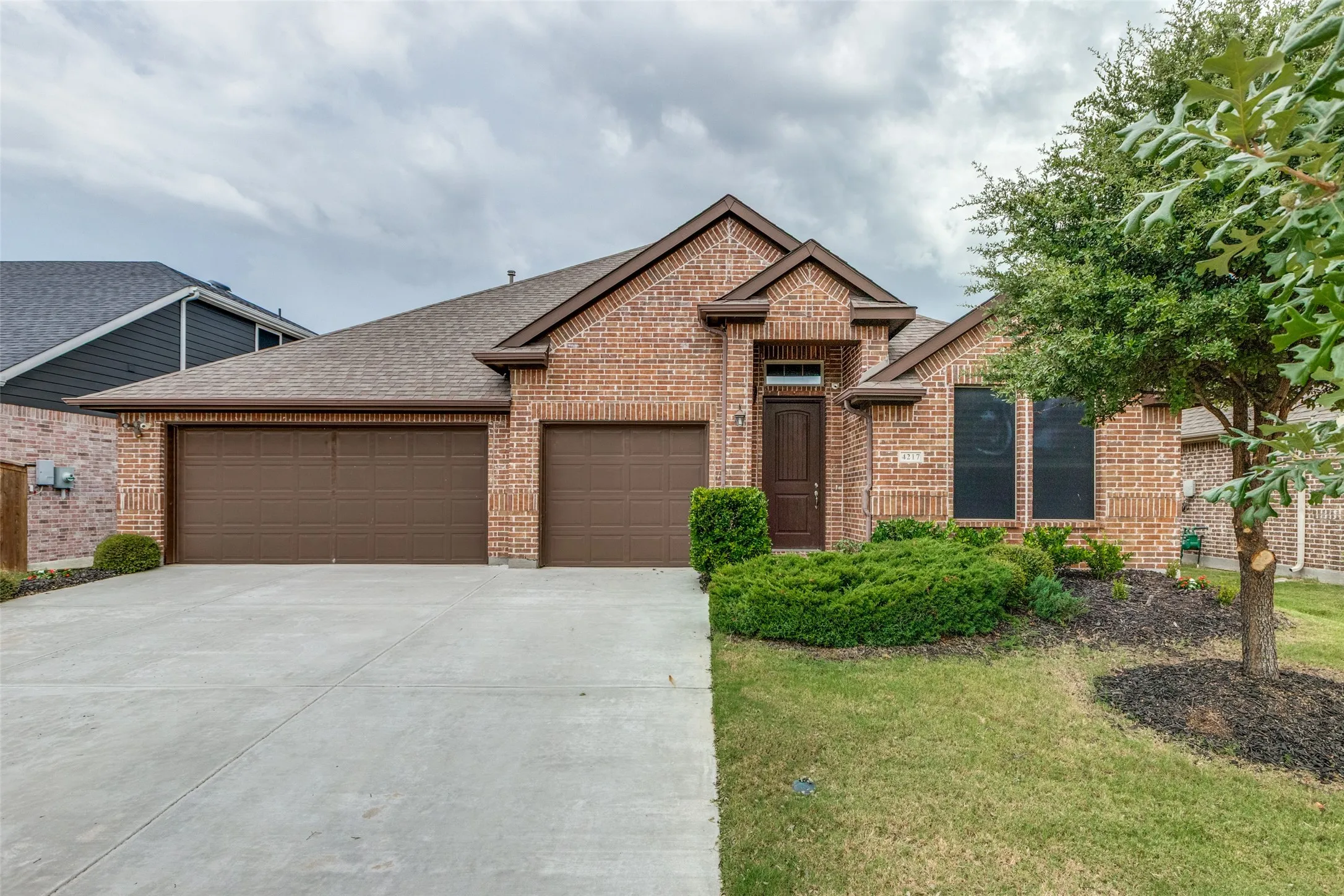 View of front of property with brick siding, roof with shingles, a garage, concrete driveway, and a front yard