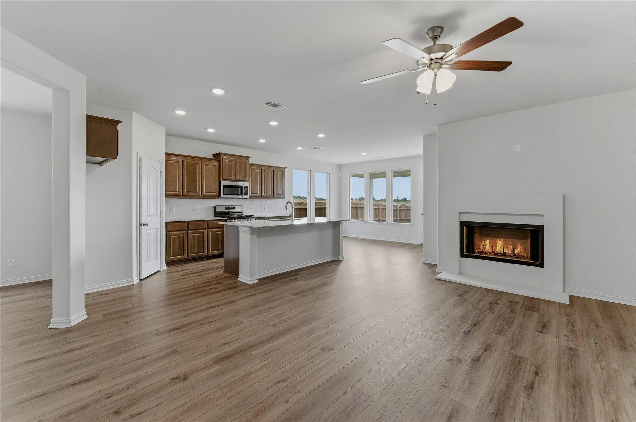 Open-concept living area with wood-finish flooring, a contemporary fireplace, and recessed lighting