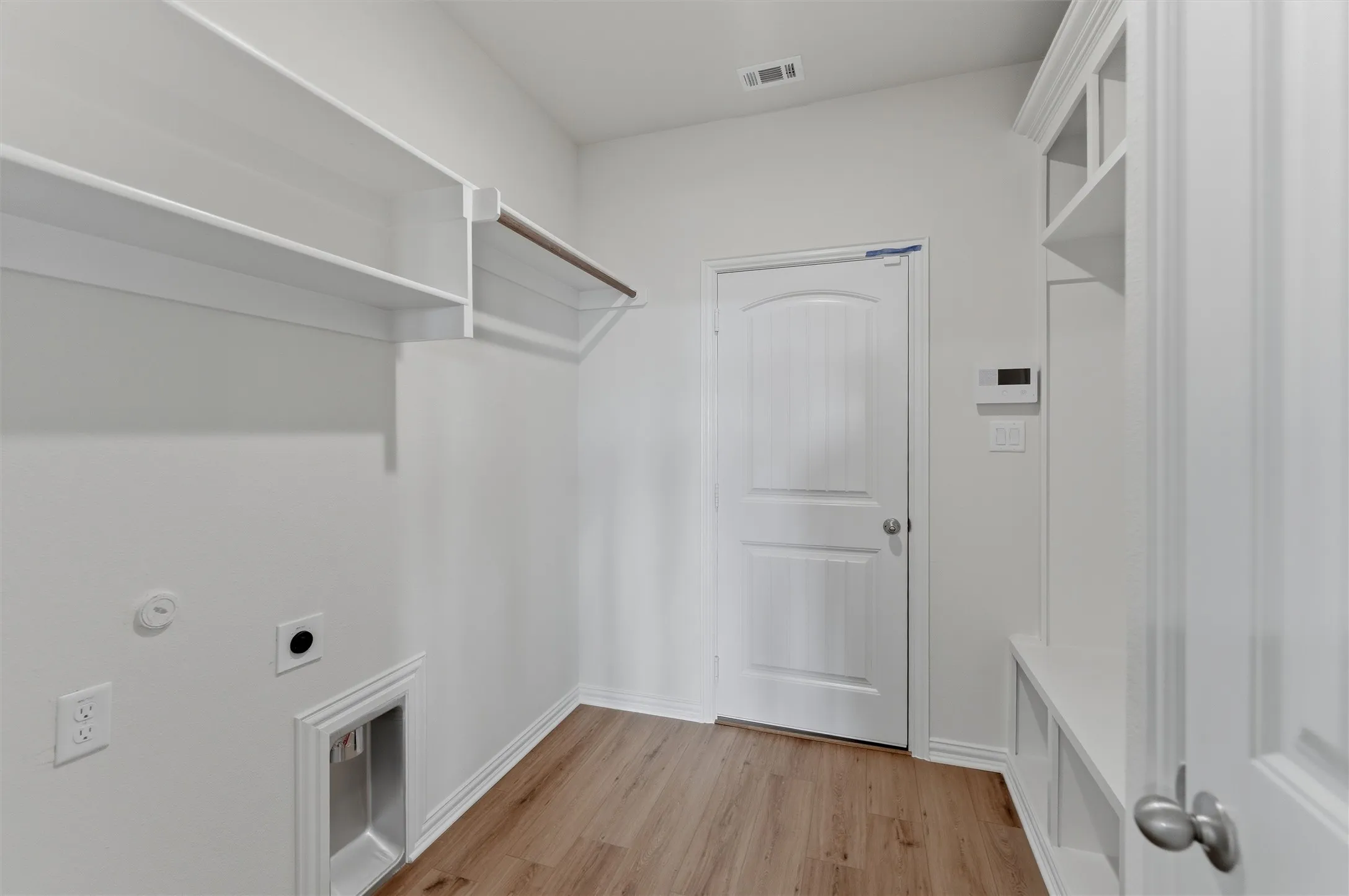 Laundry area featuring built-in shelving, hanging rod, wood-finish flooring, and a utility sink hookup