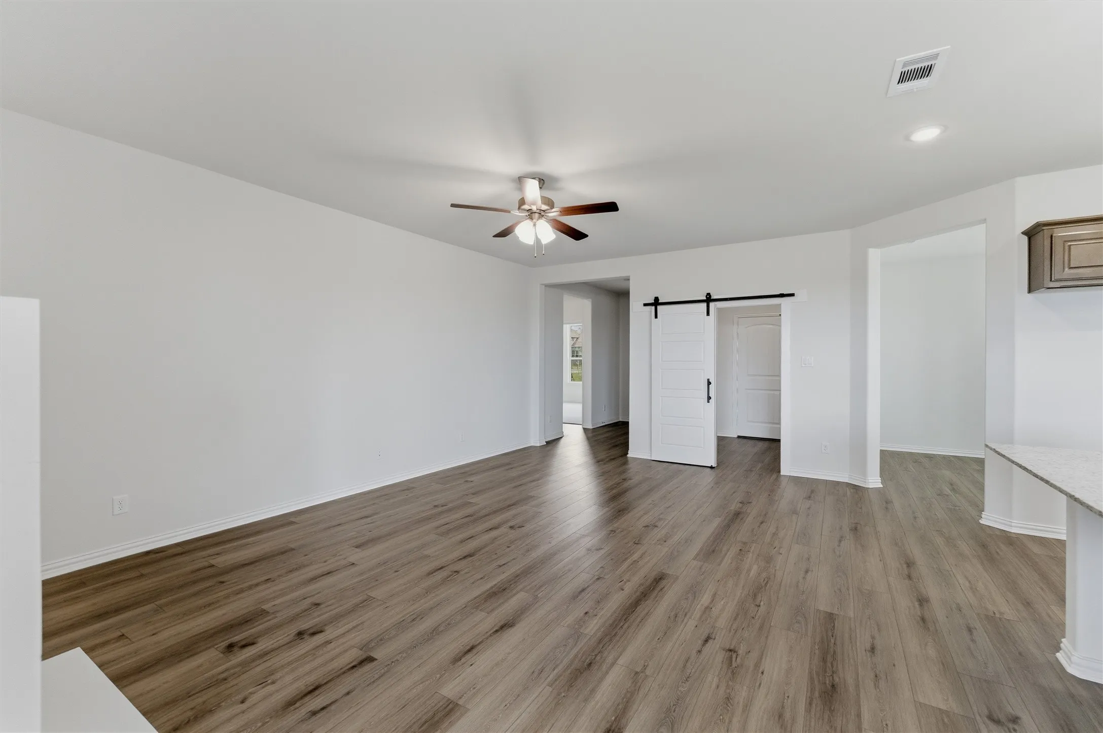Spacious room featuring wood-finish flooring, a ceiling fan with integrated lighting, and a modern white barn door