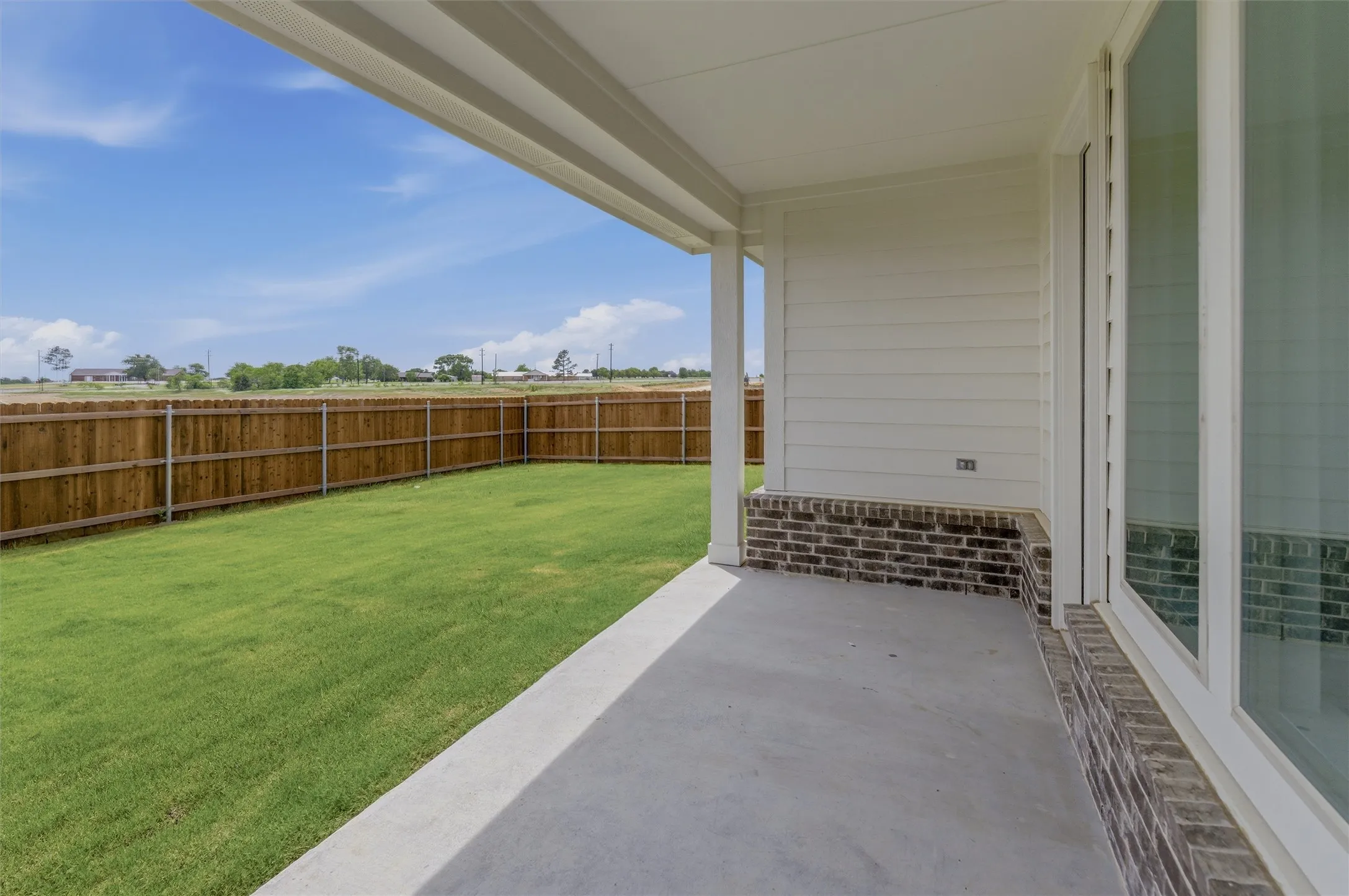 Rear patio with concrete flooring, covered ceiling, and dark brick wainscoting