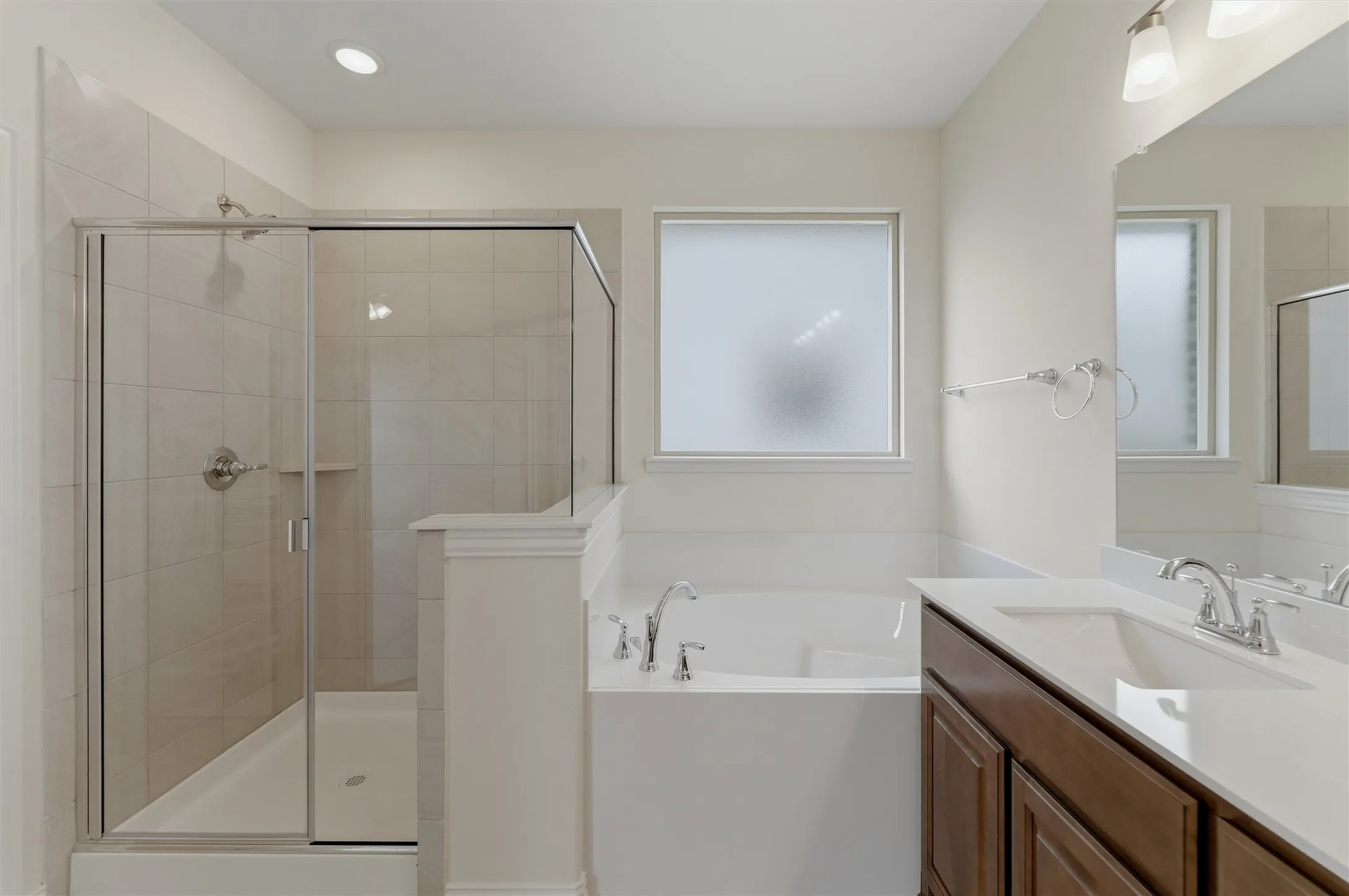 Bathroom featuring a glass-enclosed shower with tile surround, a built-in bathtub with chrome fixtures, a single vanity with a white countertop and undermount sink, a framed mirror, and a privacy window