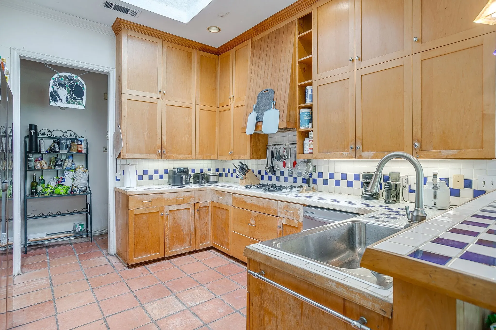 Kitchen features tile counters, abundance of cabinets, and gas stove with a skylight above