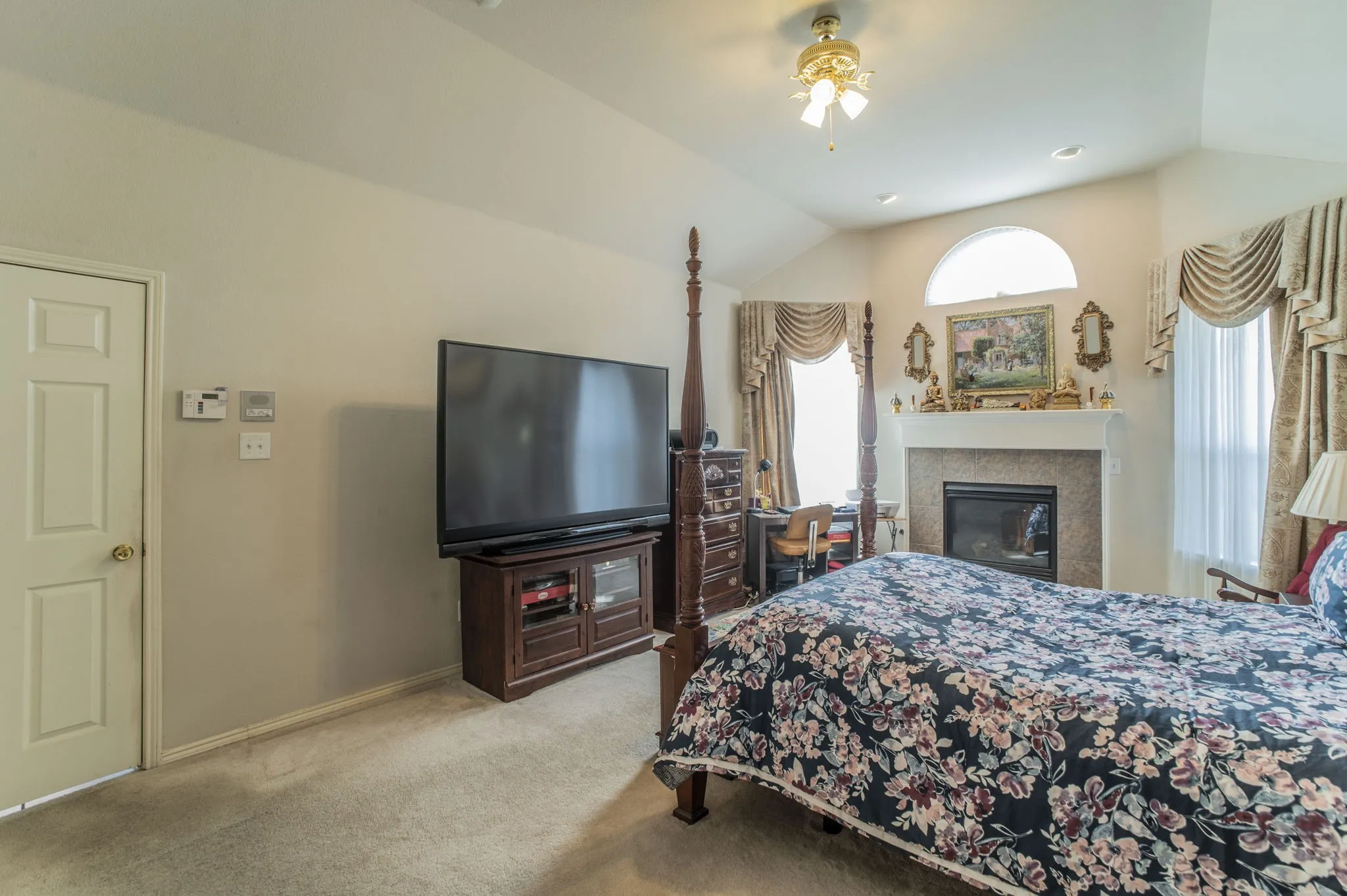 Carpeted bedroom featuring lofted ceiling, a ceiling fan, and a glass covered fireplace