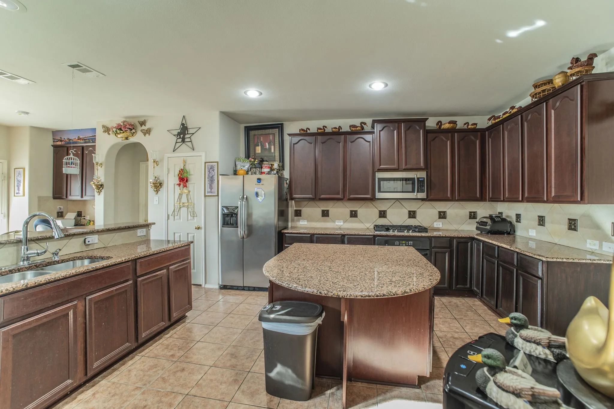 Kitchen featuring light stone counters, dark brown cabinets, hanging light fixtures, stainless steel appliances, and recessed lighting