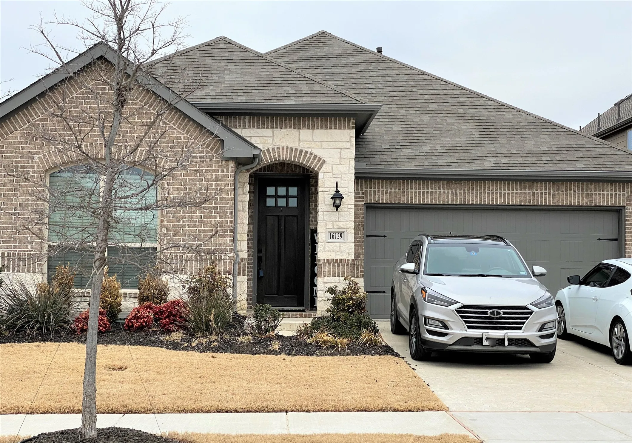 French country style house with a garage, driveway, roof with shingles, stone siding, and brick siding