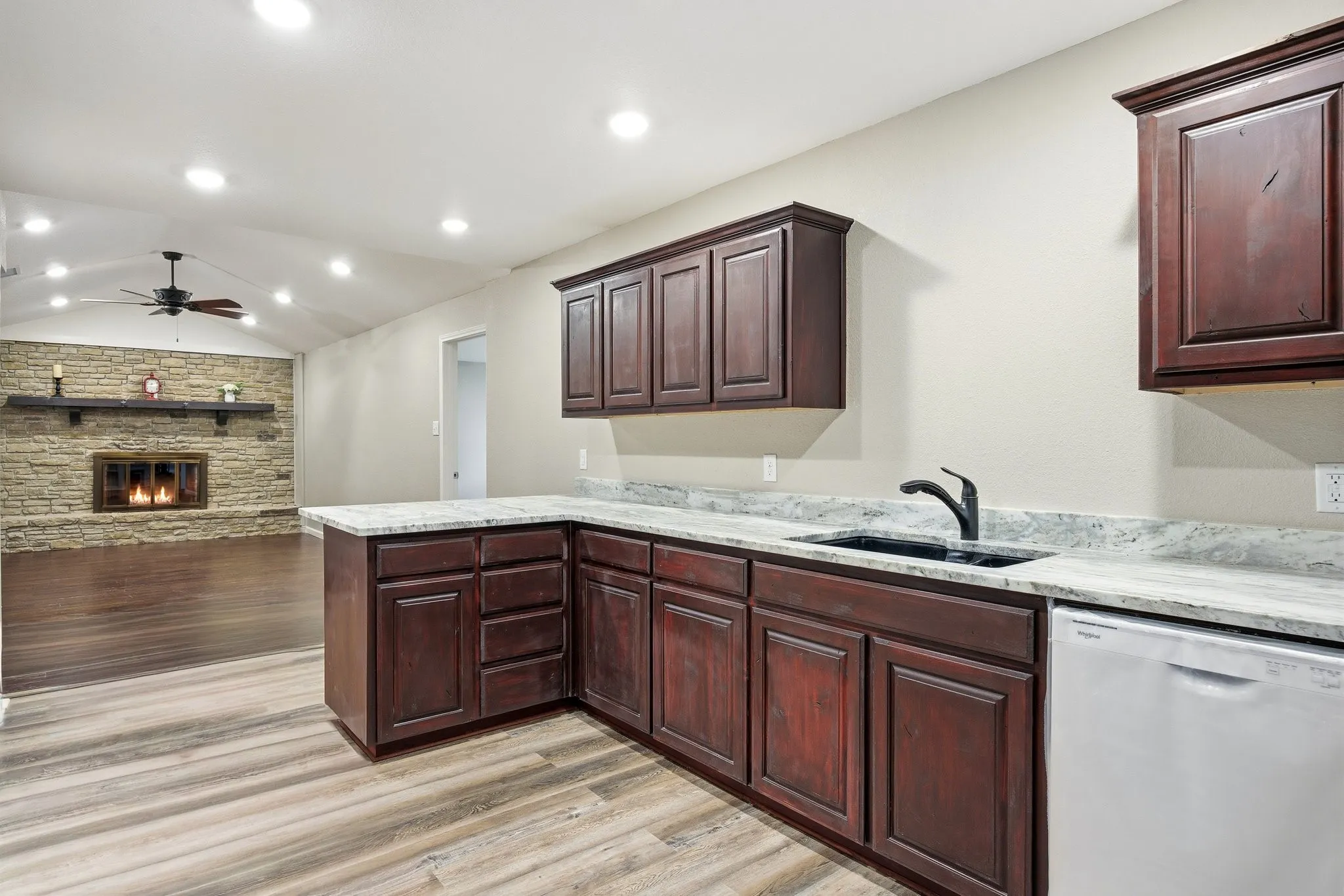 Kitchen featuring lofted ceiling, dishwasher, a fireplace, a peninsula, and light granite countertops