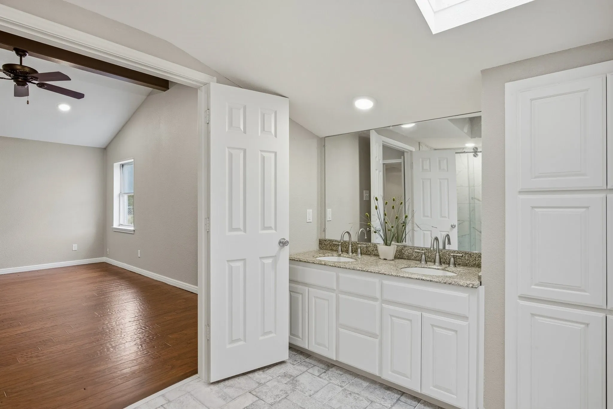 Full bath with double vanity, a skylight, recessed lighting, and light wood-style floors