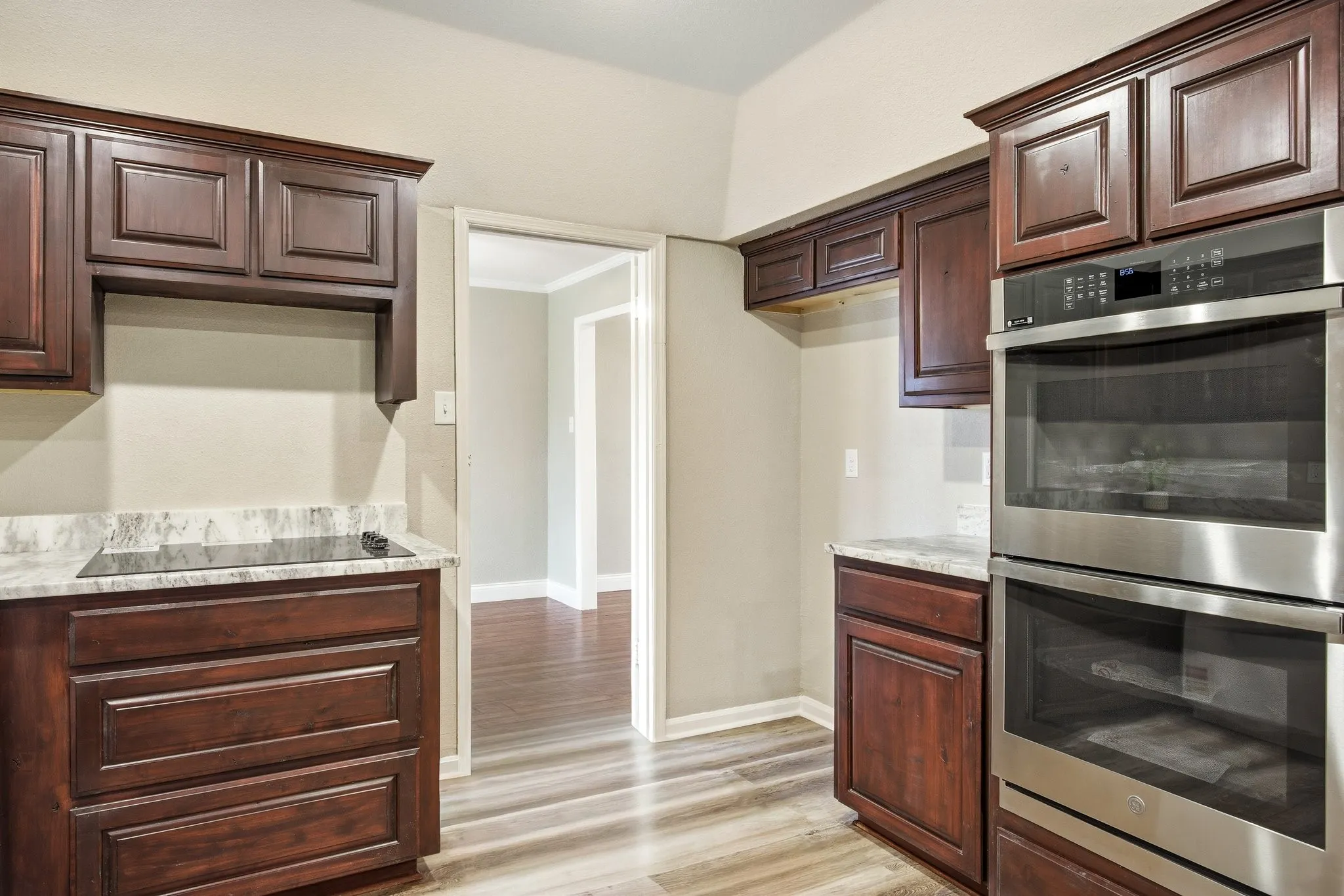 Kitchen featuring stainless steel double oven, light wood finished floors, ornamental molding, dark brown cabinetry, and black electric cooktop
