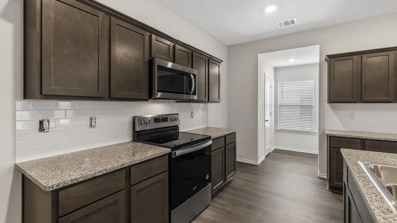 Kitchen with appliances with stainless steel finishes, dark brown cabinetry, dark wood-type flooring, tasteful backsplash, and light stone countertops