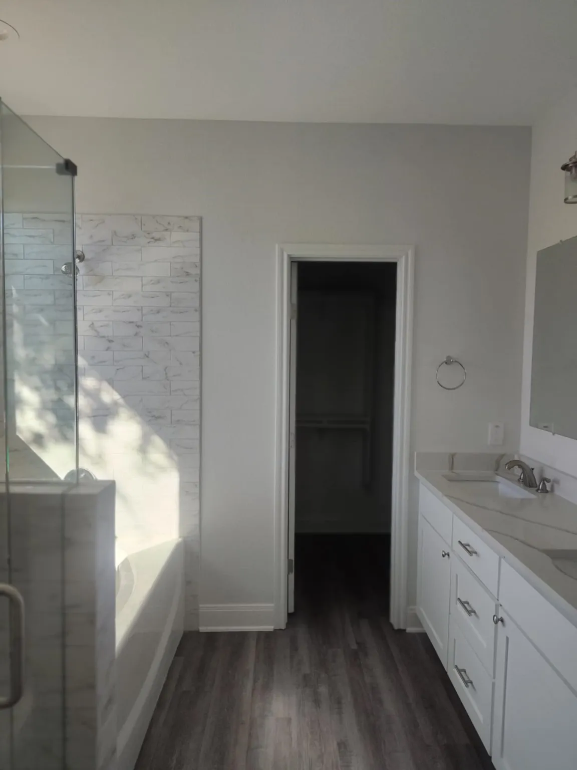 Full bathroom featuring a bath, double vanity, a shower stall, a spacious closet, and dark wood-type flooring