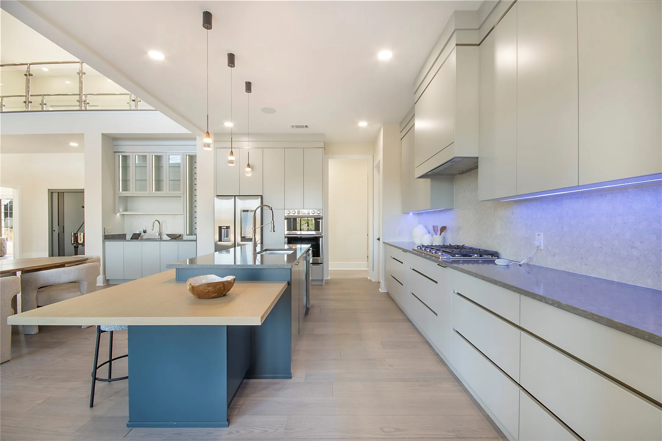 Kitchen featuring modern cabinets, a center island with sink, decorative light fixtures, appliances with stainless steel finishes, and a kitchen bar