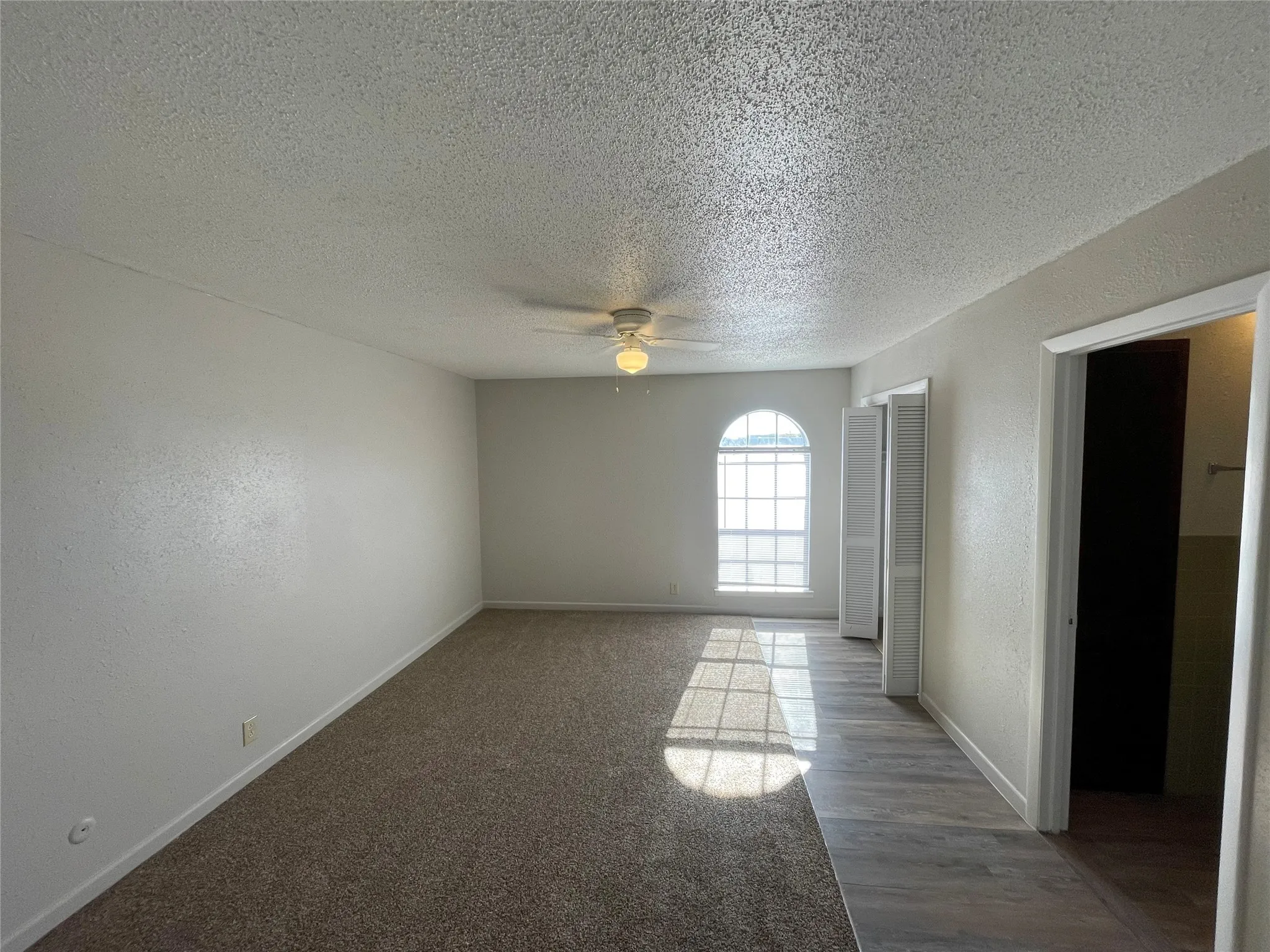 Carpeted spare room with a textured ceiling, a textured wall, and ceiling fan