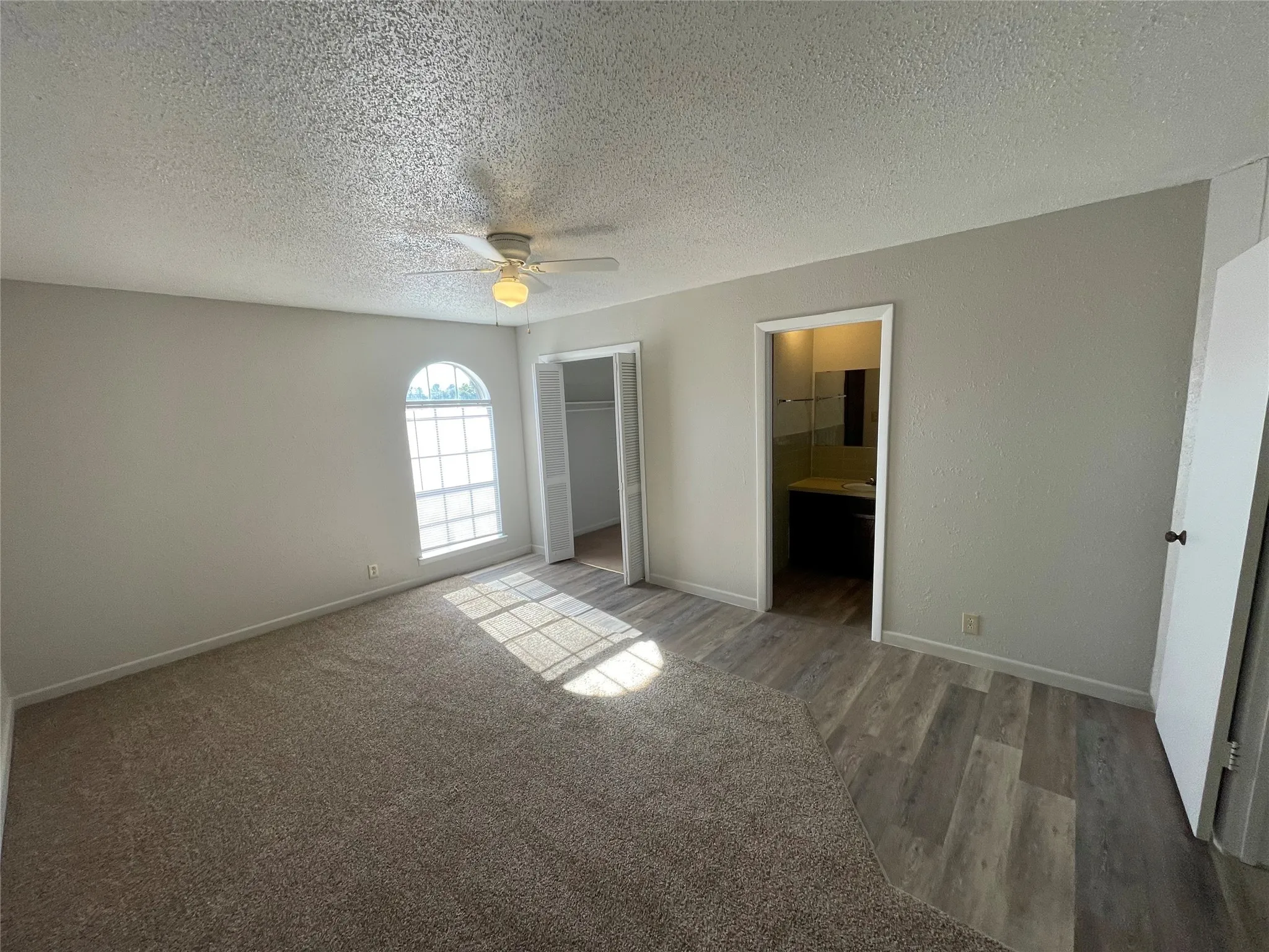 Unfurnished bedroom with ceiling fan, a textured ceiling, light wood-style floors, and a walk in closet