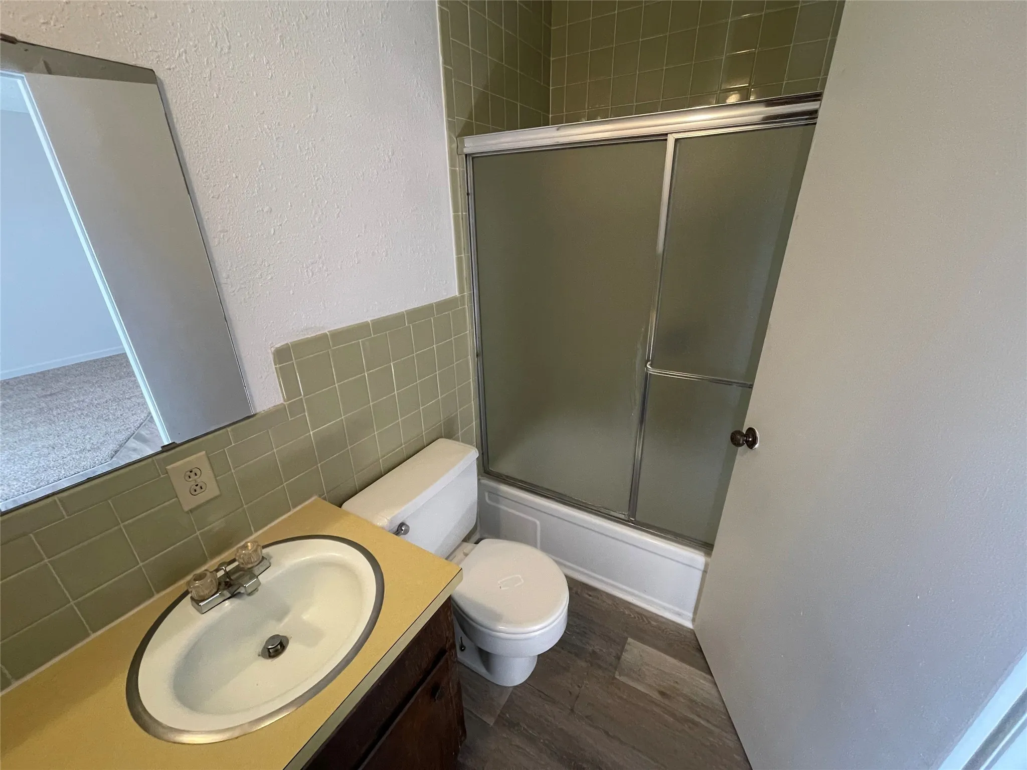 Bathroom featuring a textured wall, tile walls, vanity, enclosed tub / shower combo, and dark wood-style flooring