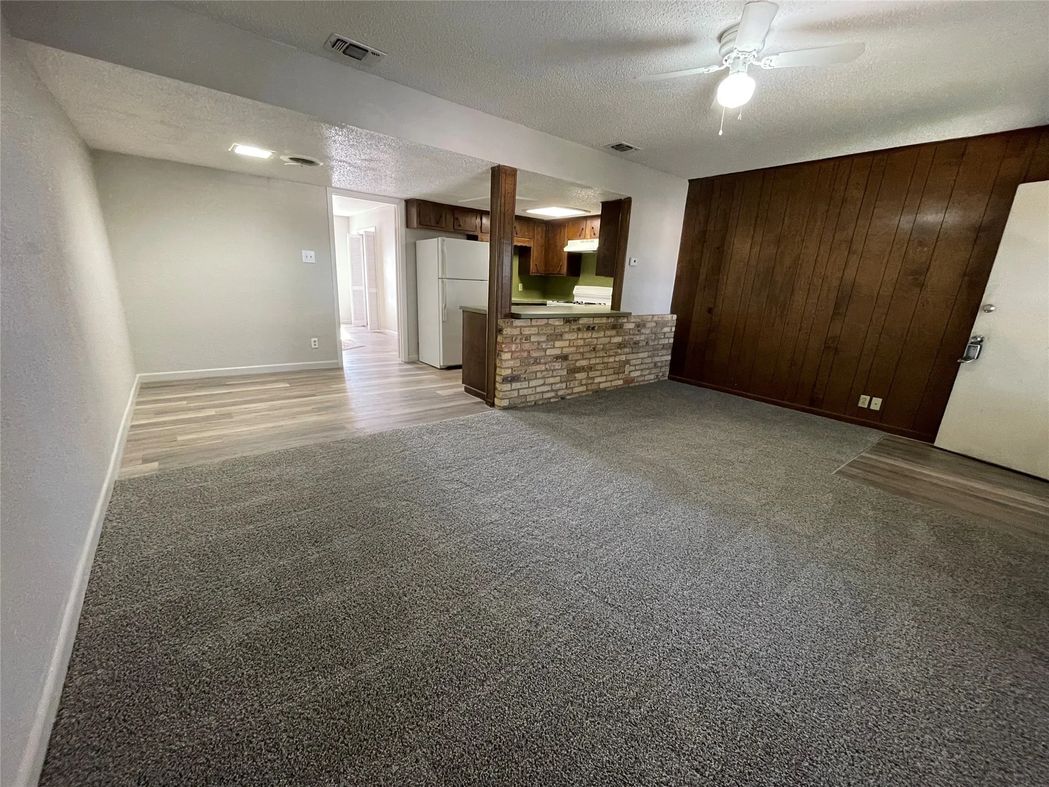 Unfurnished living room featuring a textured ceiling, light carpet, wooden walls, a ceiling fan, and an accent wall