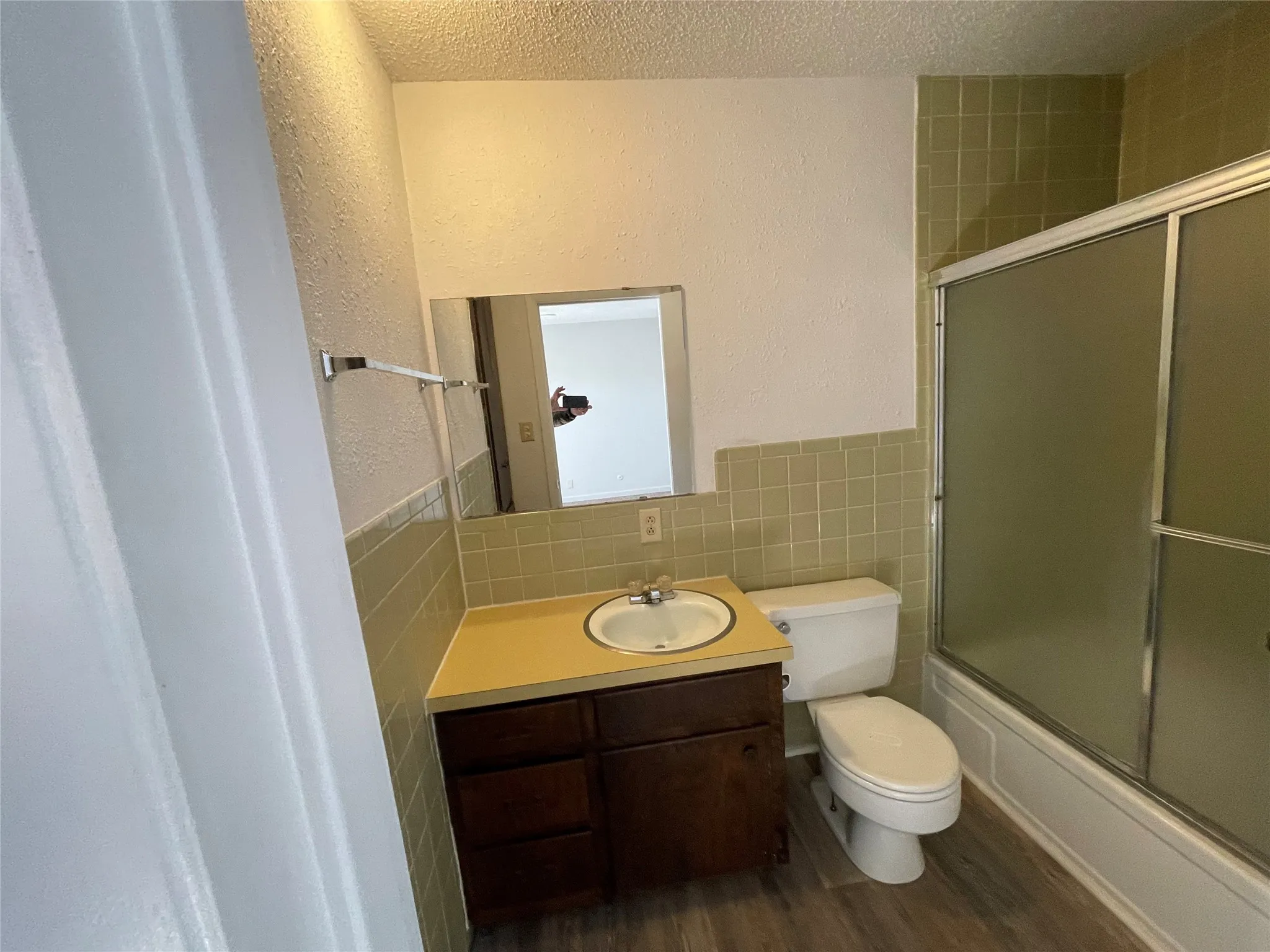 Bathroom with shower / bath combination with glass door, tile walls, a wainscoted wall, a textured ceiling, and a textured wall