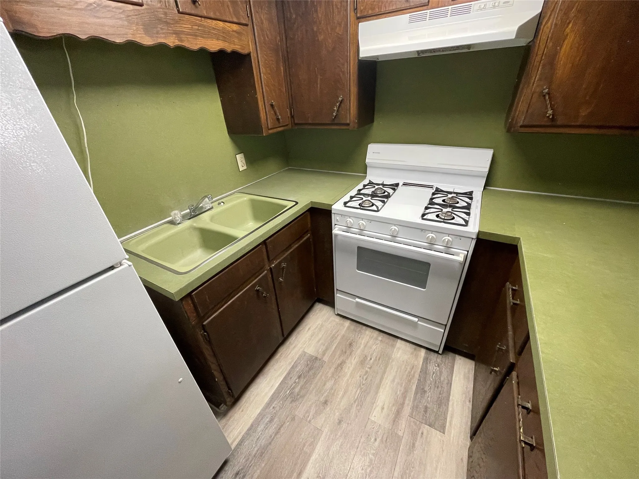 Kitchen with white appliances, under cabinet range hood, dark brown cabinetry, light wood-style floors, and light countertops
