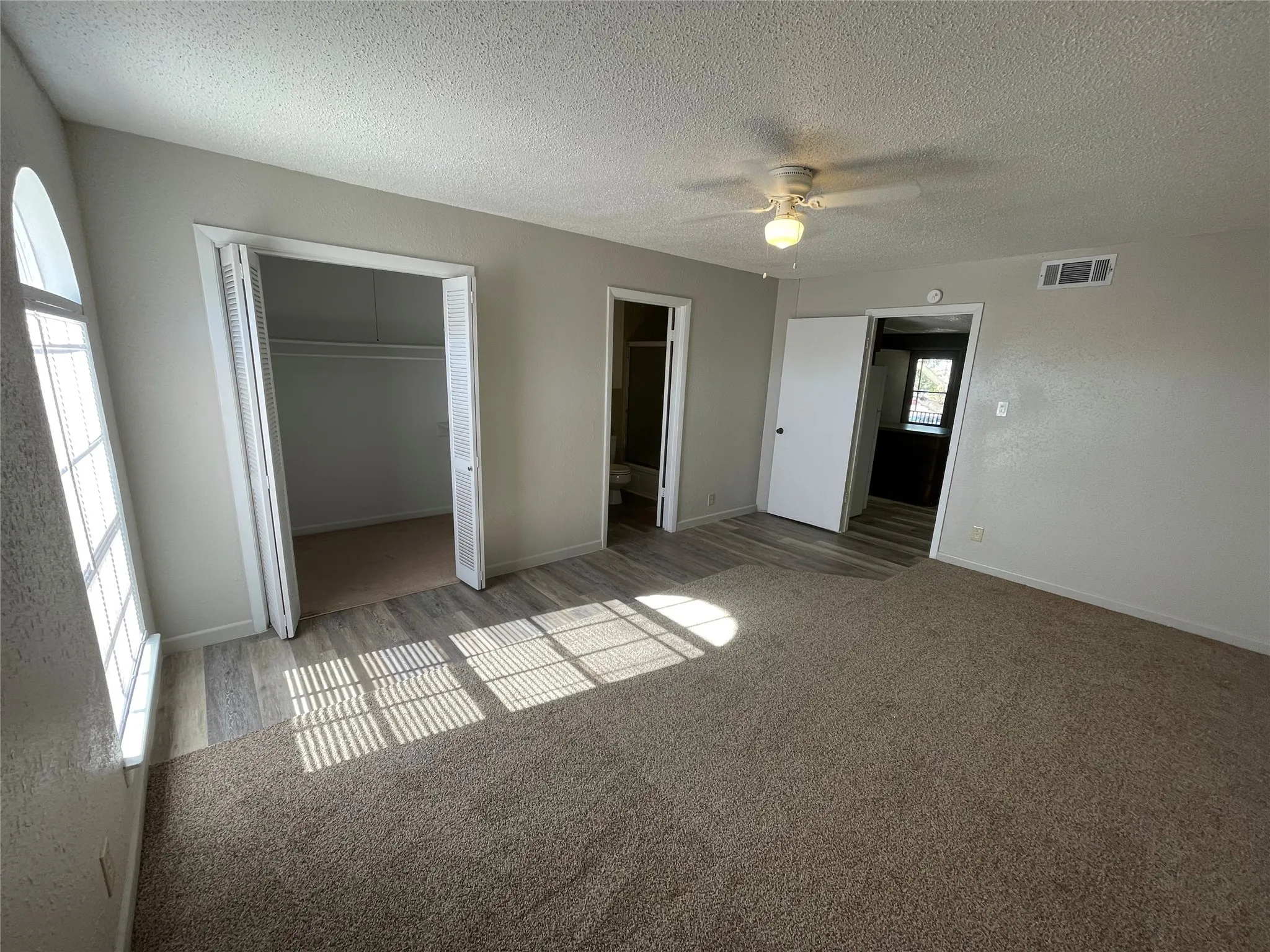 Unfurnished bedroom with a textured ceiling, a closet, carpet, ceiling fan, and ensuite bathroom