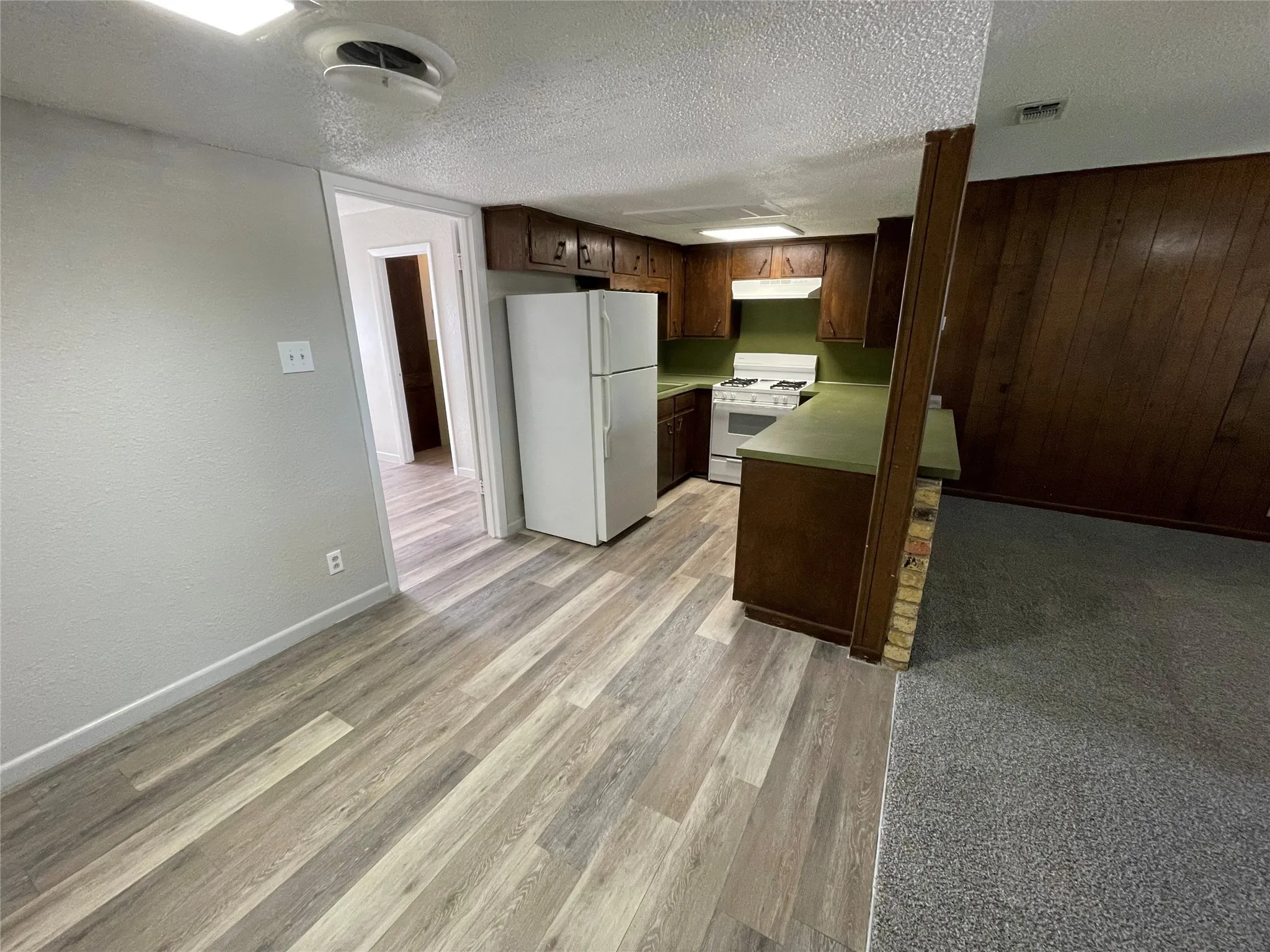 Kitchen featuring white appliances, a textured ceiling, light countertops, dark brown cabinets, and light wood-style floors