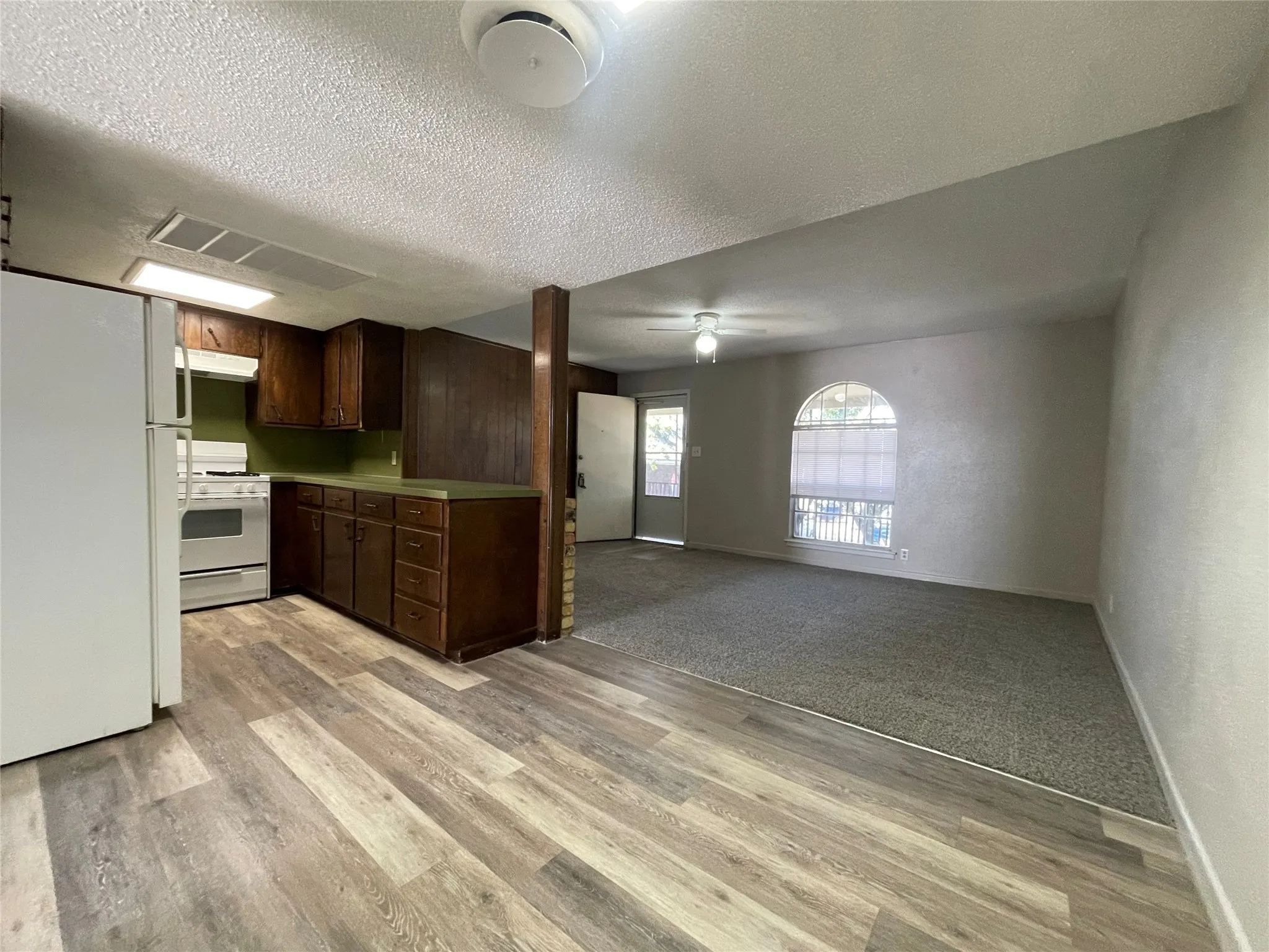 Kitchen with white appliances, light countertops, dark brown cabinetry, a textured ceiling, and open floor plan