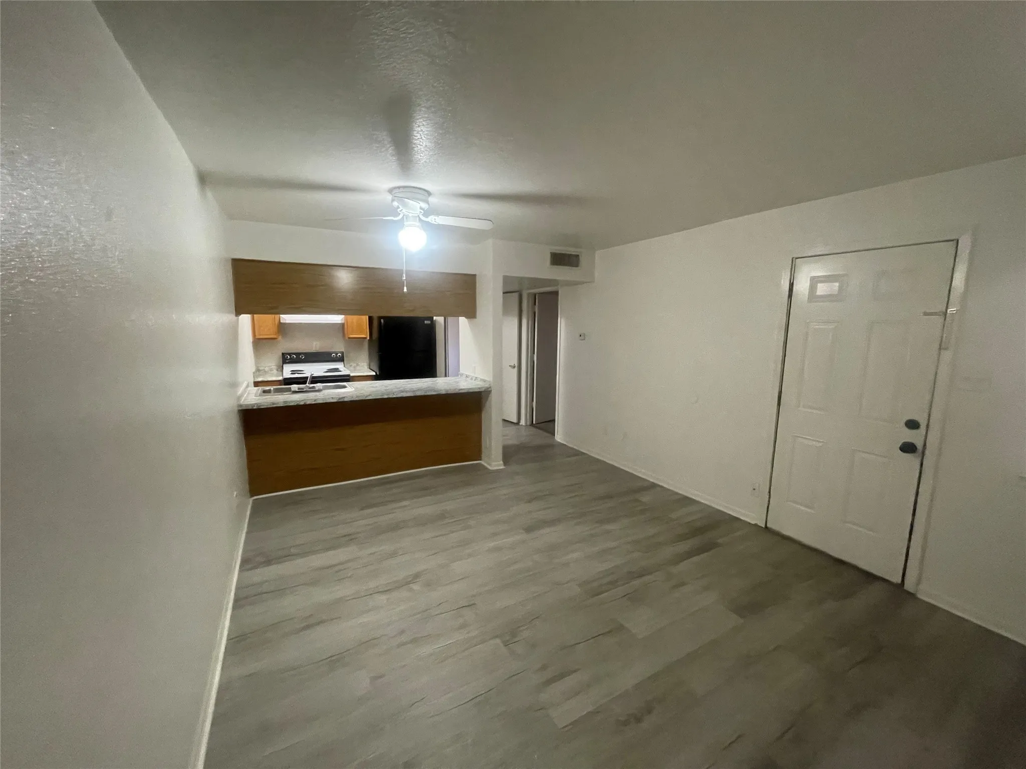 Unfurnished living room featuring dark wood-style flooring, a ceiling fan, and a textured ceiling