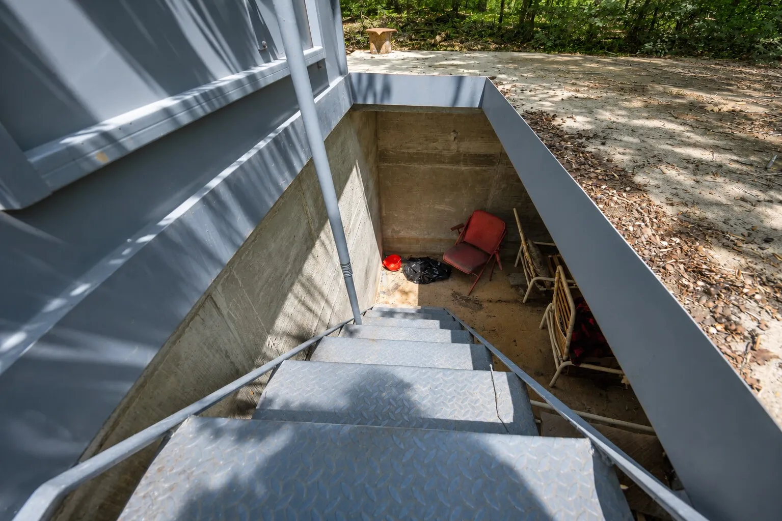 Exterior basement access featuring metal stairs with handrails, concrete walls, and a recessed outdoor area