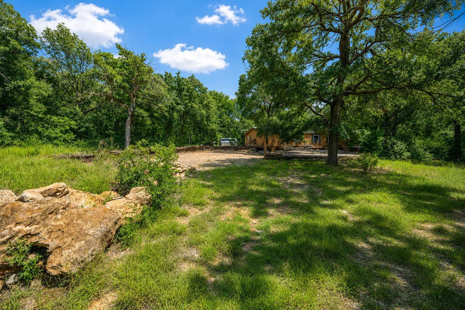 Expansive outdoor space featuring a stone wall, mature trees, a grassy lawn, and a natural landscape