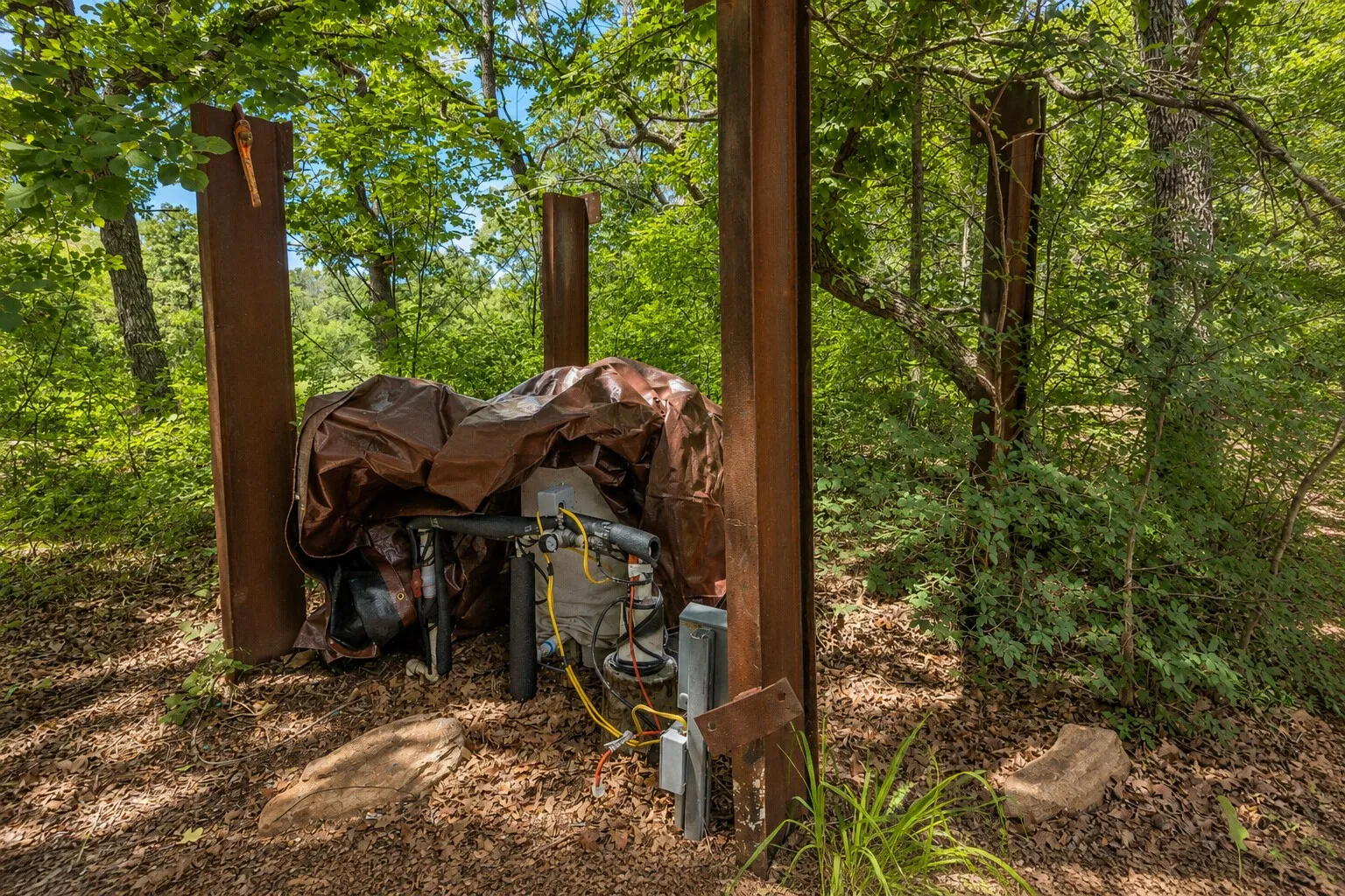 Utility equipment, partially covered, positioned within a wooded setting