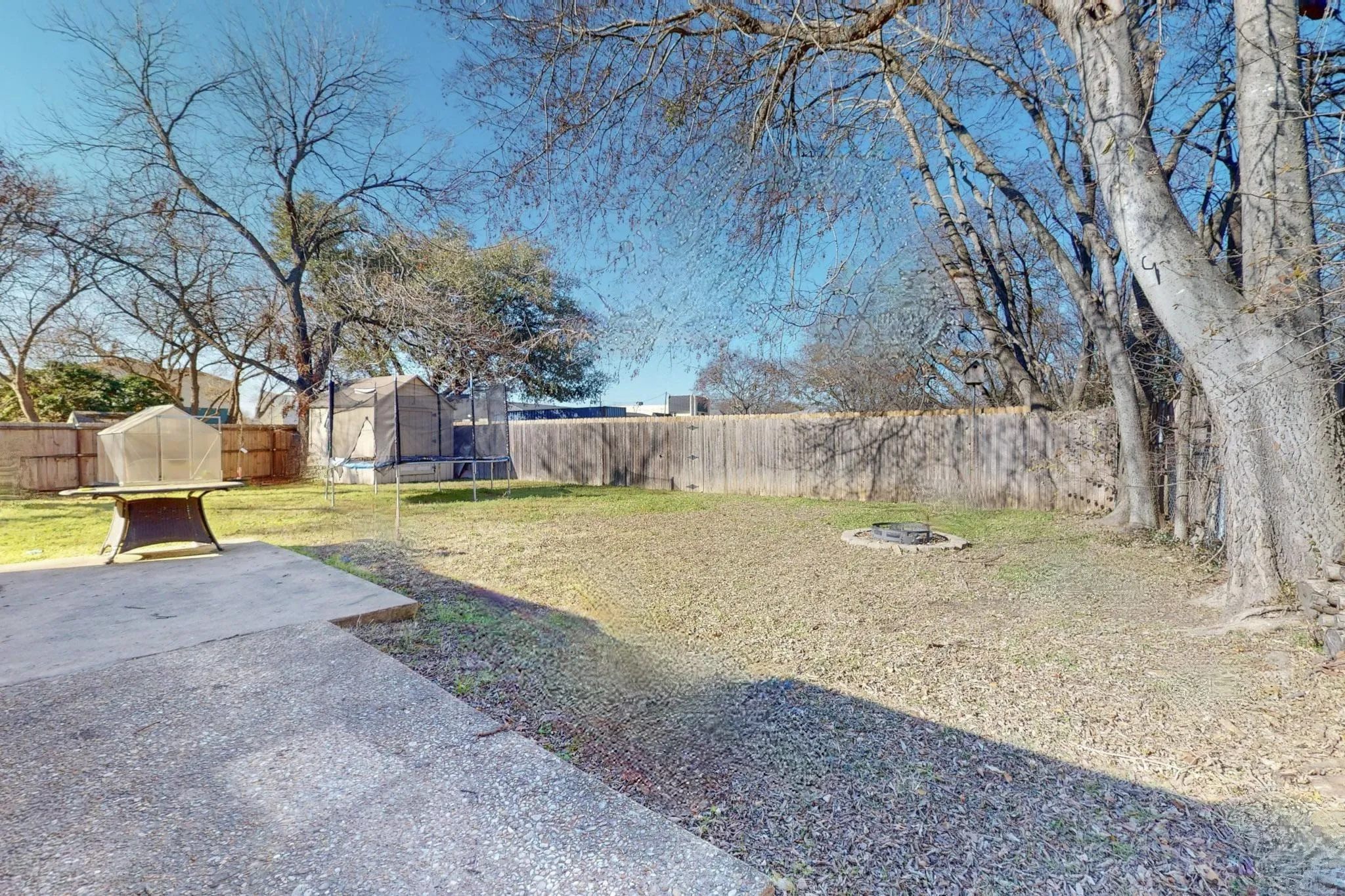 Fenced backyard with a trampoline and an outdoor fire pit