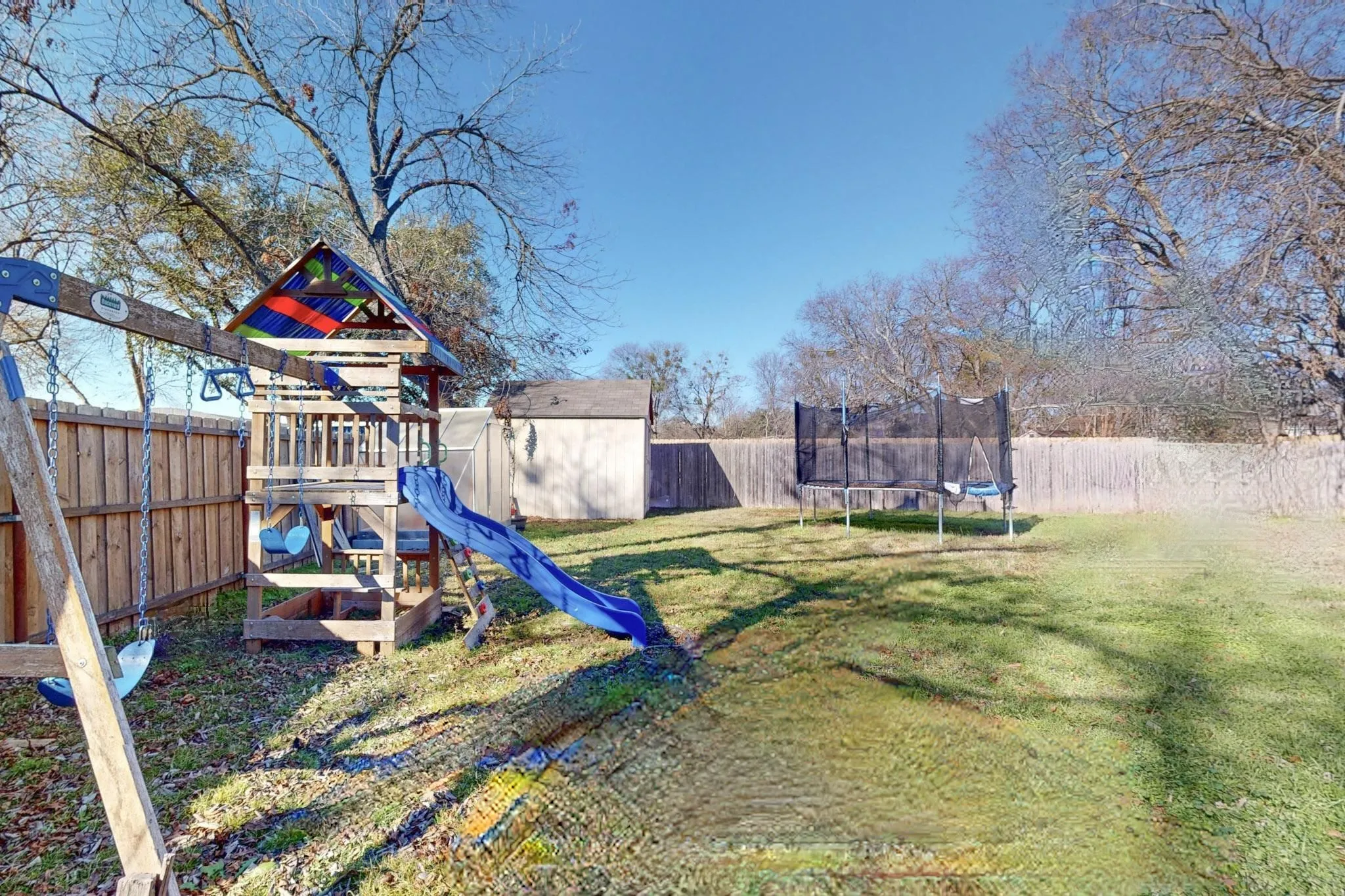 View of jungle gym featuring a trampoline, a fenced backyard, and a storage unit