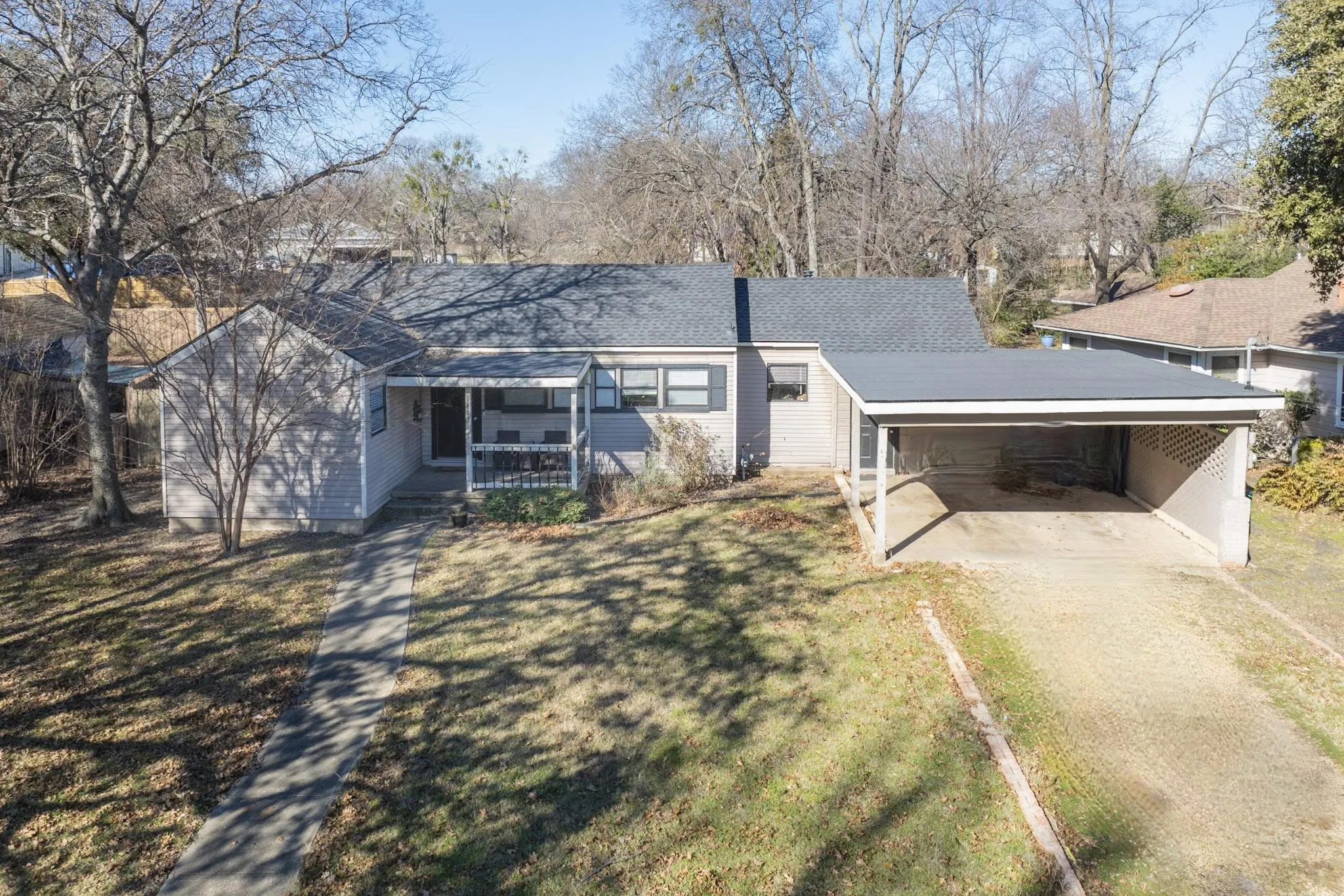 Ranch-style house featuring driveway, covered porch, a front lawn, and an attached carport