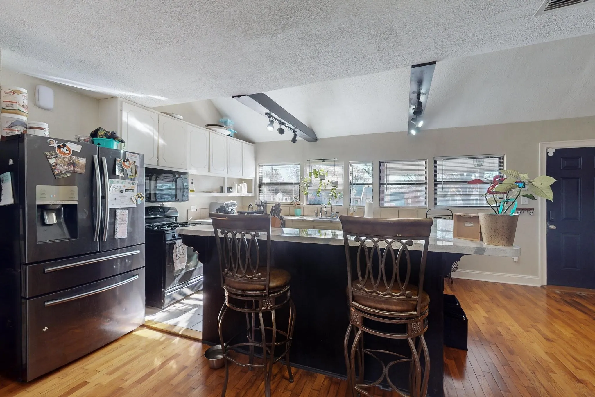 Kitchen featuring black appliances, white cabinetry, lofted ceiling, light wood-style flooring, and a textured ceiling