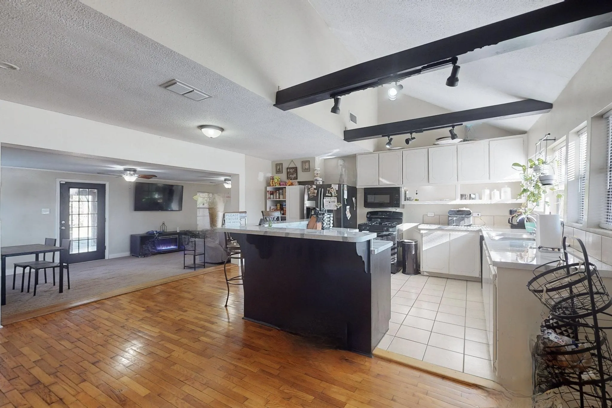 Kitchen featuring white cabinets, a textured ceiling, a breakfast bar, rail lighting, and black appliances