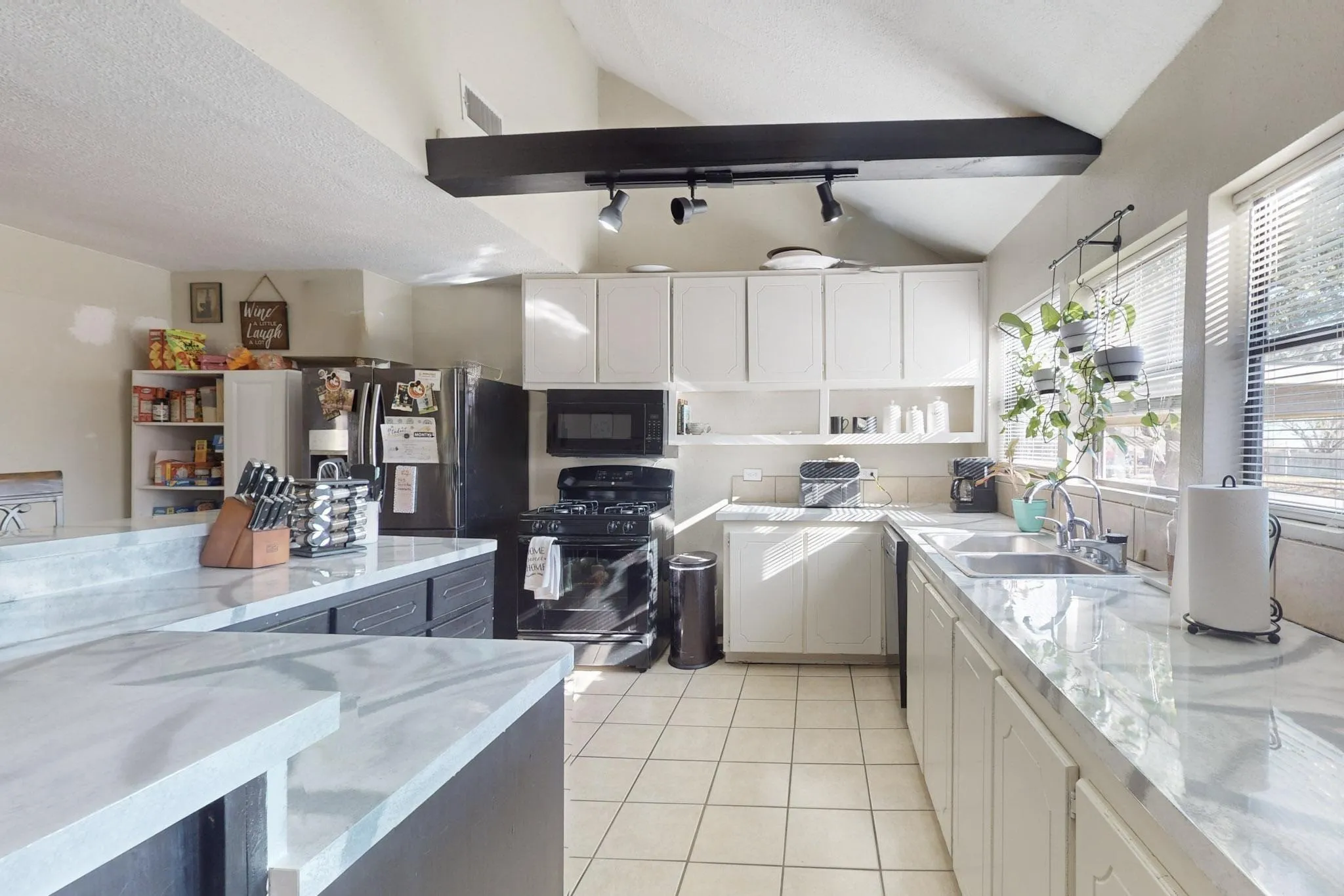 Kitchen with black appliances, white cabinets, lofted ceiling, rail lighting, and light tile patterned floors