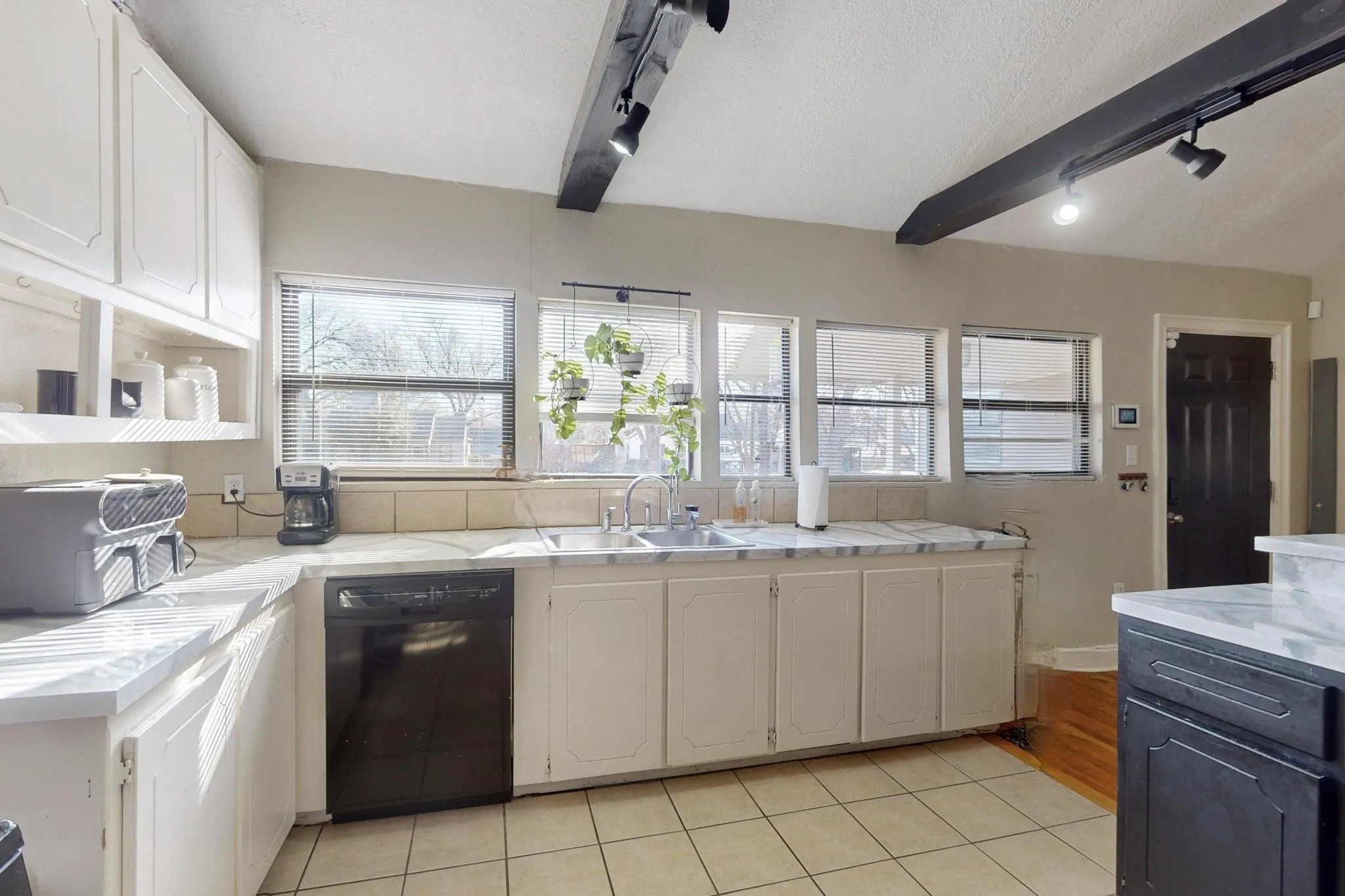 Kitchen with track lighting, white cabinetry, black dishwasher, healthy amount of natural light, and beam ceiling