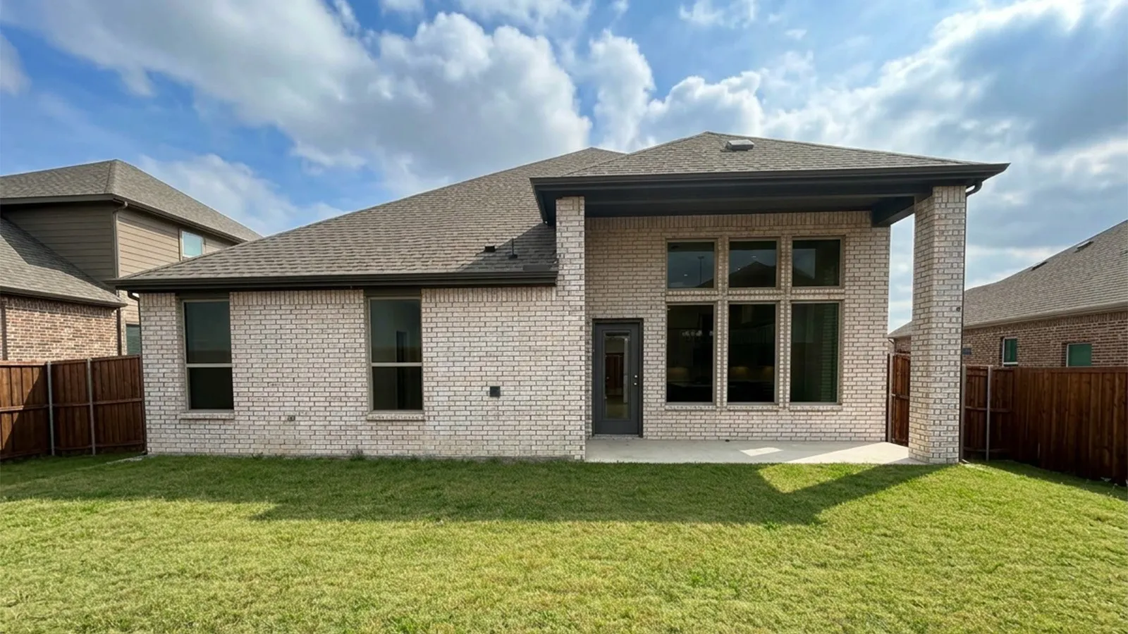 Rear exterior featuring light-colored brick, a covered patio, and multi-pane windows